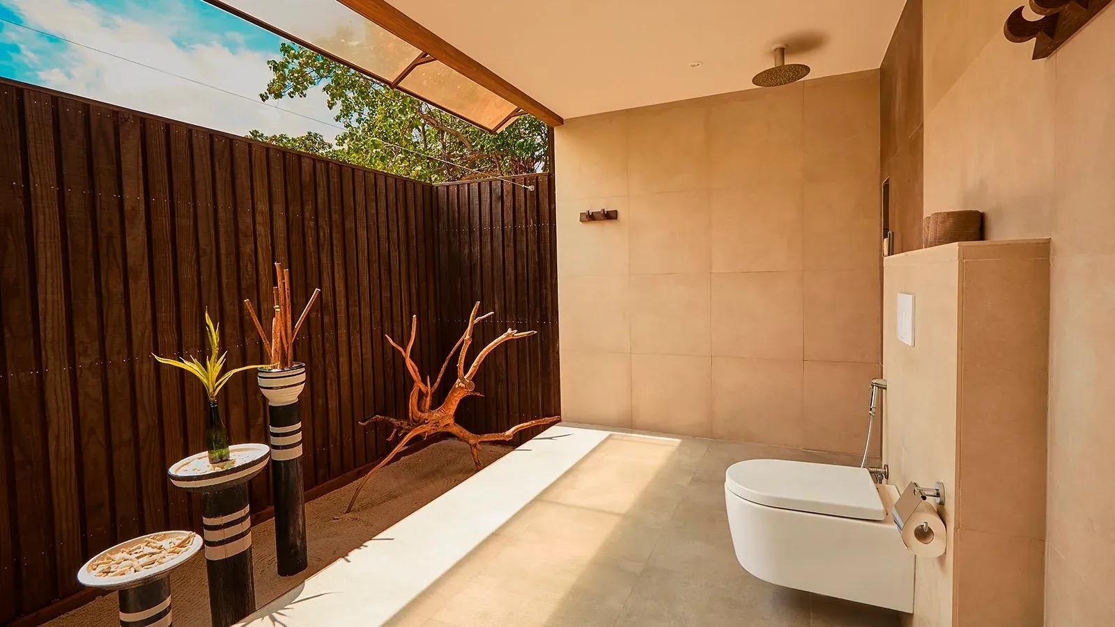 Bagno all'aperto della Deluxe Beach Villa con doccia a pioggia e arredi naturali al Kuredu Island Resort & Spa.