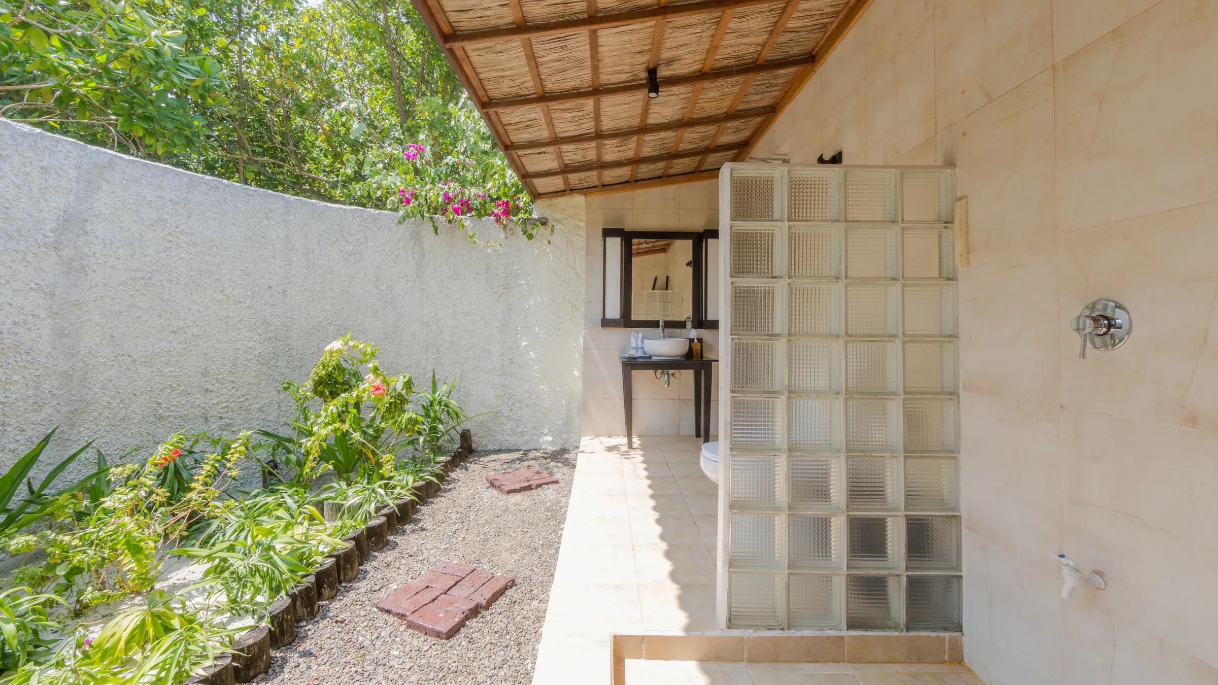 Giardino con vegetazione, parete divisoria in vetro e lavandino nella Garden Bungalow del Kuredu Island Resort & Spa.