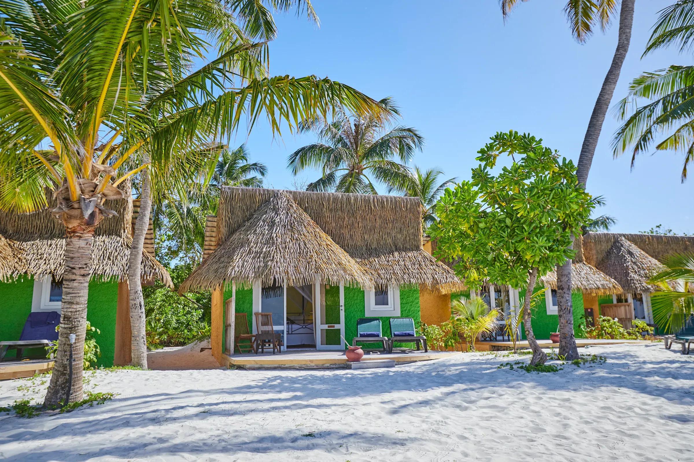Bungalow sulla spiaggia con tetto in paglia e sedute esterne, circondato da palme nella Premium Beach Bungalow del Kuredu Island Resort & Spa.