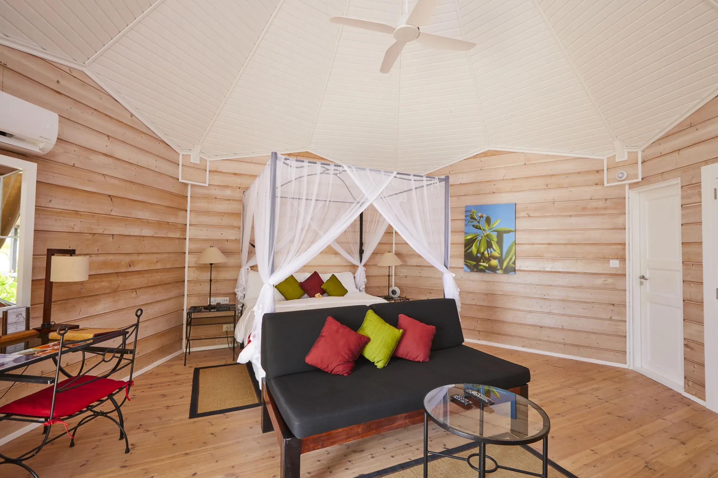 Interno della Premium Beach Villa con letto a baldacchino, divano e tavolo al Kuredu Island Resort & Spa.