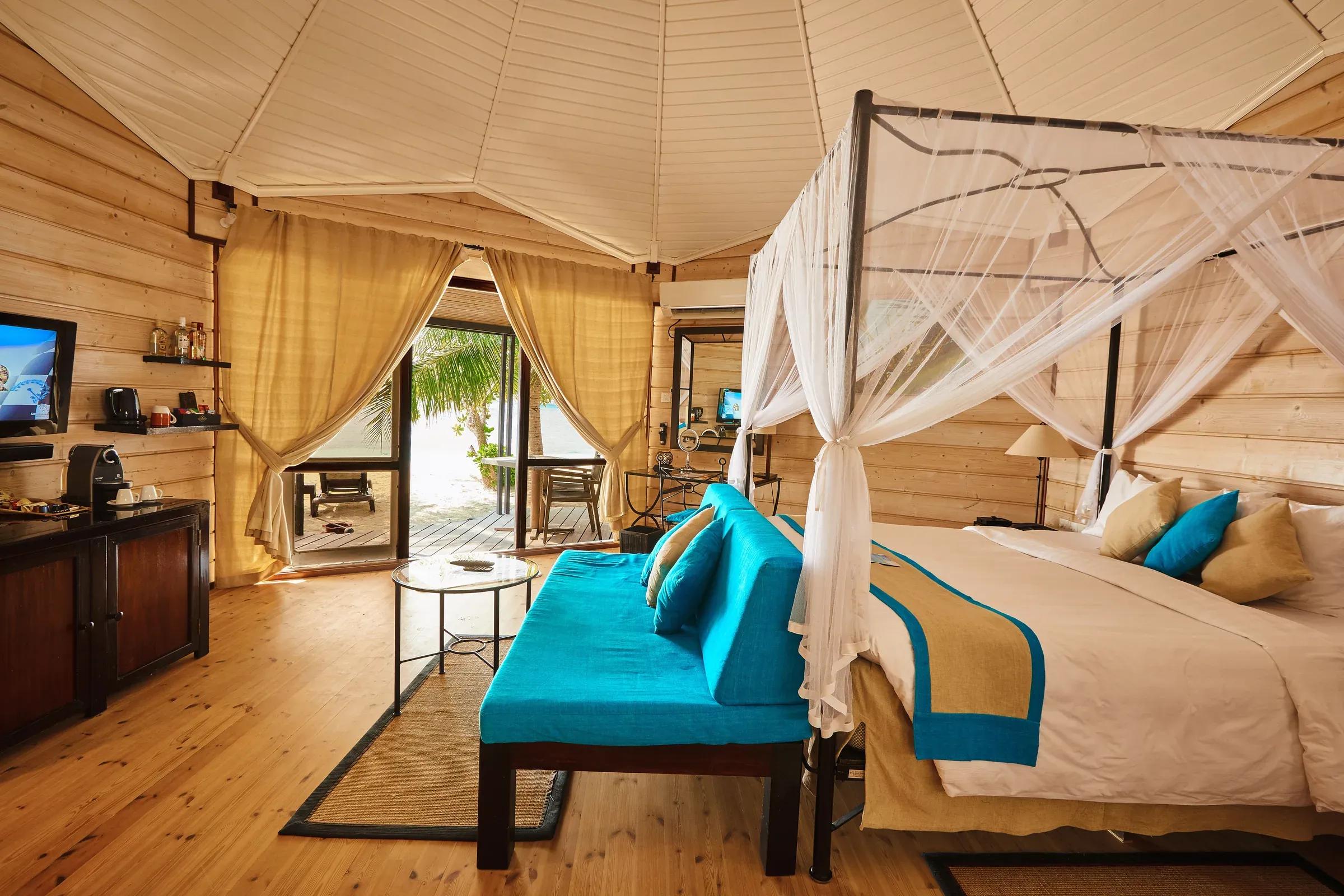 Interno della Sangu Jacuzzi Beach Villa con letto a baldacchino e divano presso Kuredu Island Resort & Spa.
