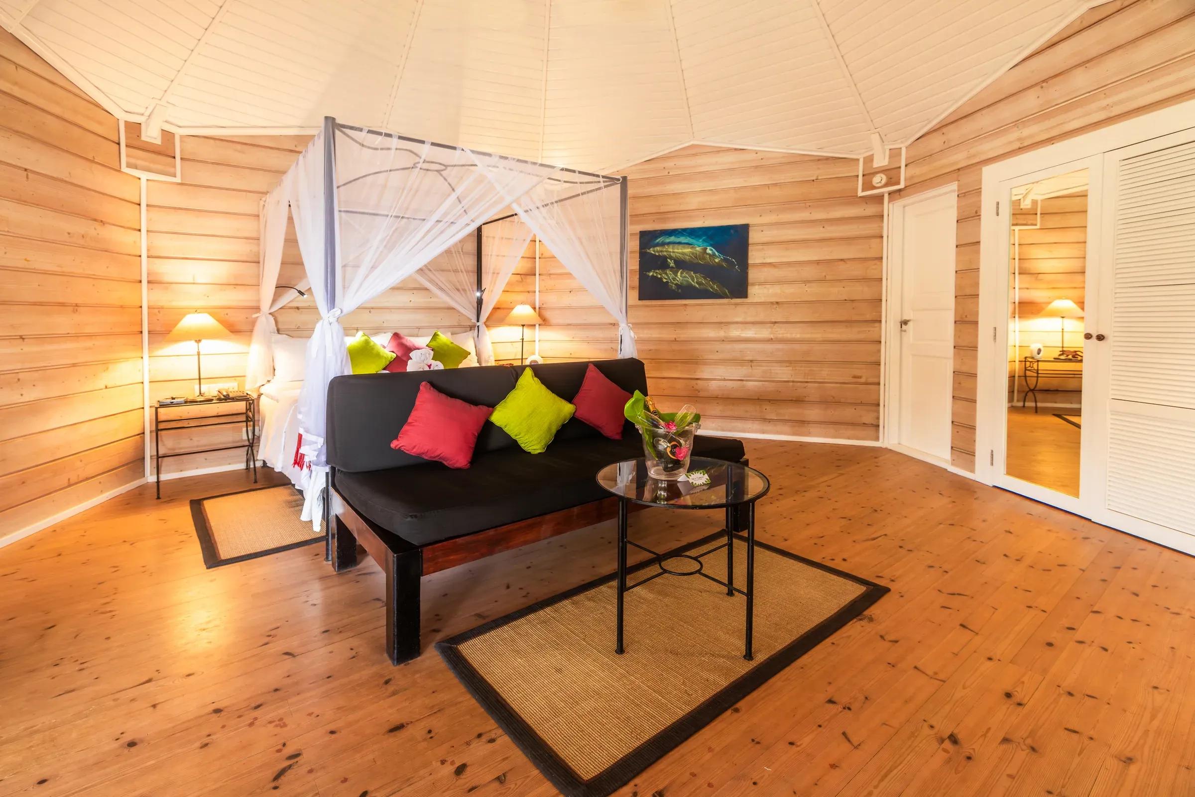 Interno della Sangu Premium Beach Villa con letto a baldacchino e divano colorato al Kuredu Island Resort & Spa.