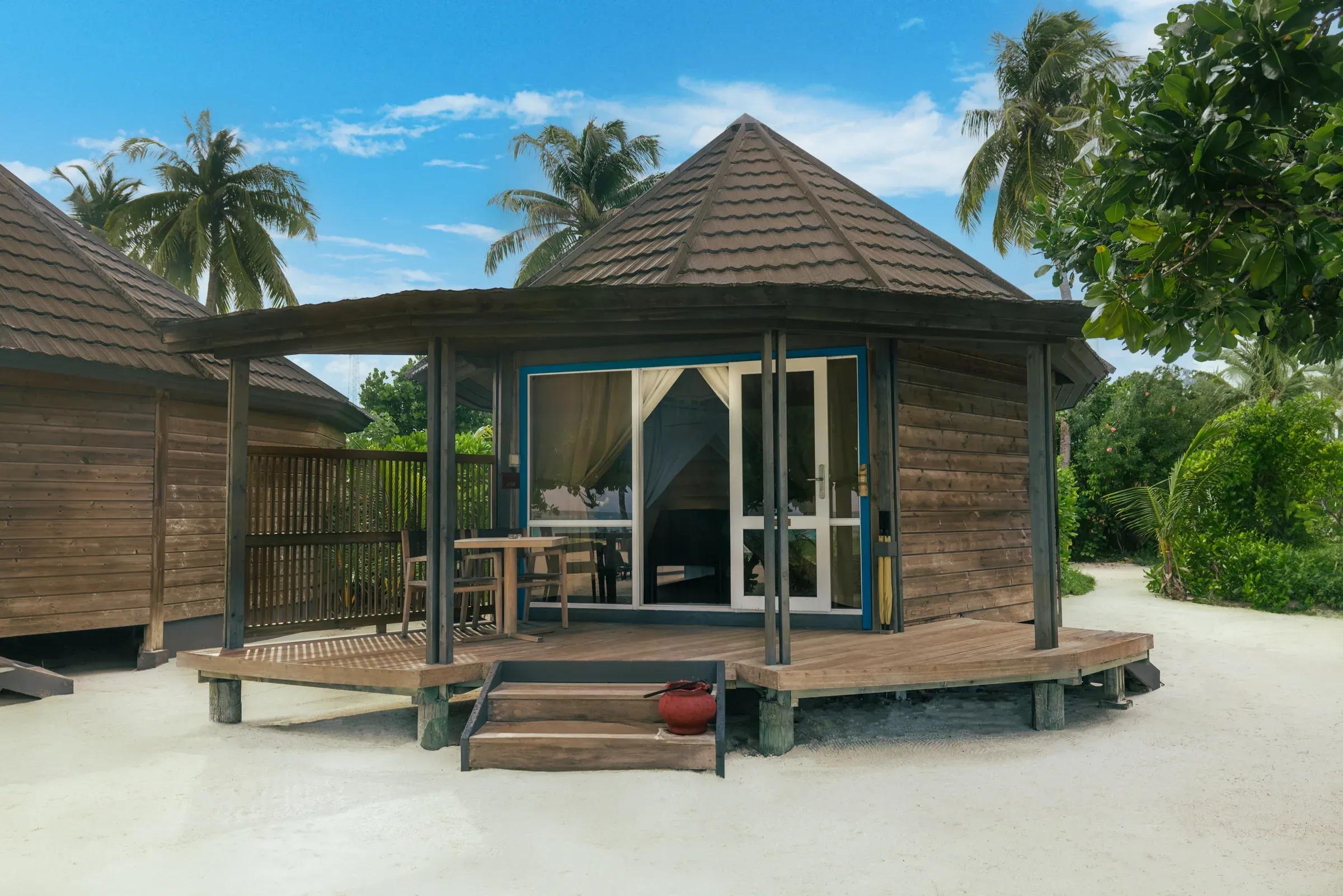 Veranda della Sangu Premium Beach Villa con tavolo e sedie in legno, circondata da alberi presso Kuredu Island Resort & Spa.