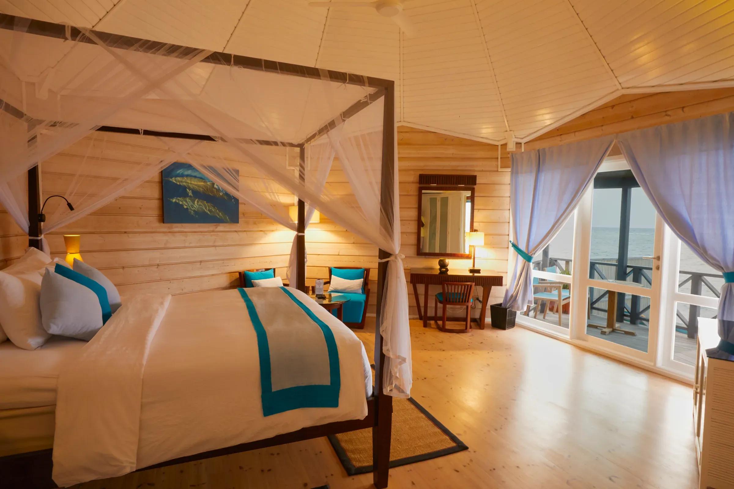 Camera della Sangu Water Villa con letto a baldacchino, scrivania e vista mare al Kuredu Island Resort & Spa.