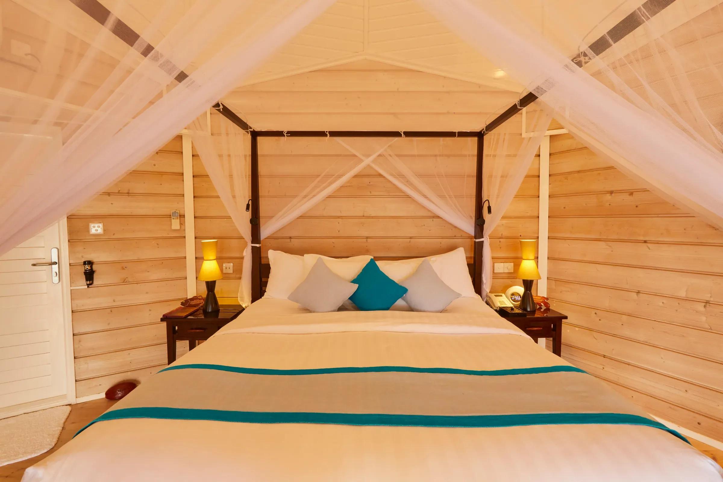 Interno della Sangu Water Villa con letto matrimoniale a baldacchino e lampade presso Kuredu Island Resort & Spa.