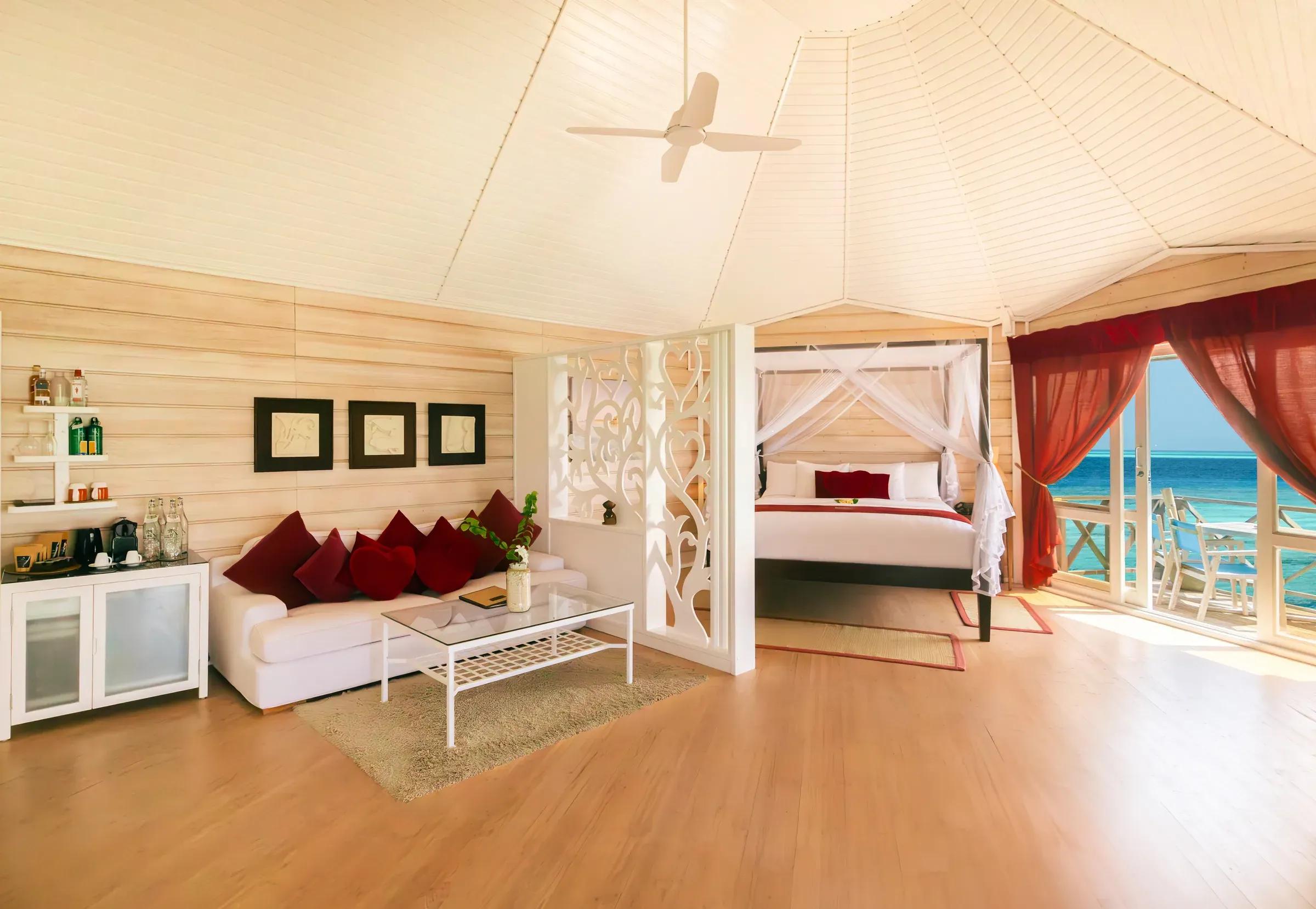 Interno della Sangu Water Villa Honeymoon Suite con salotto, letto a baldacchino e vista mare al Kuredu Island Resort & Spa.
