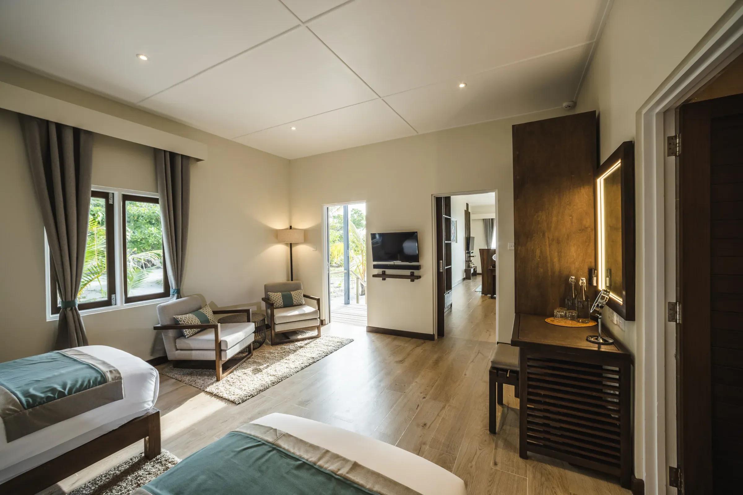 Interno della Two Bedroom Beach Villa con sedie, finestra e accesso al patio verde del Kuredu Island Resort & Spa.