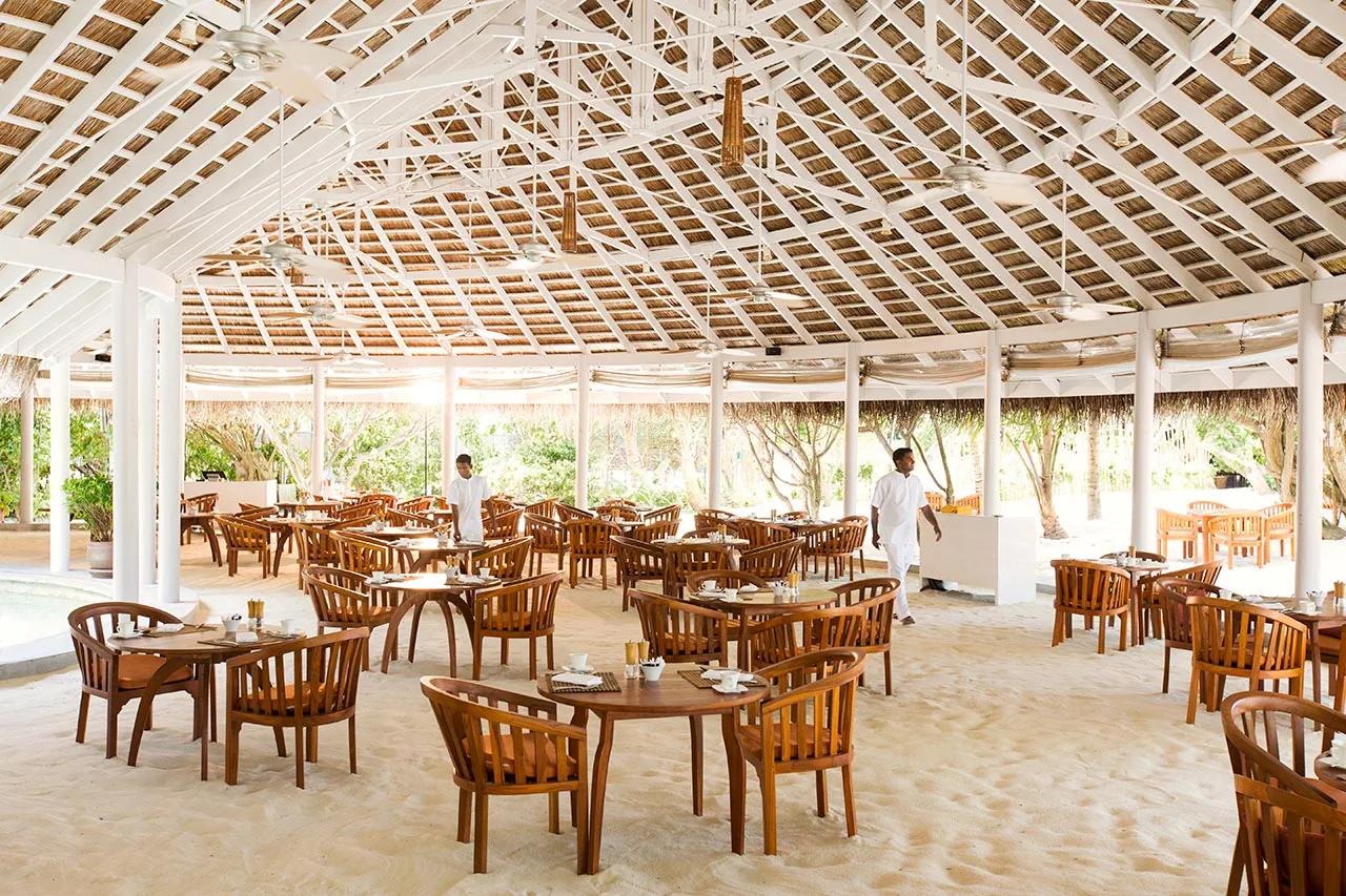 Sala ristorante con tavoli in legno e pavimento di sabbia al LUX* South Ari Atoll