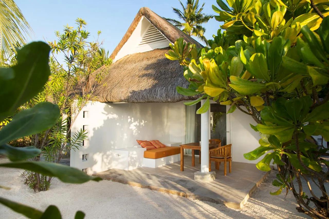 Esterno della Beach Pavilion con divano e tavolo in legno circondato da vegetazione al LUX* South Ari Atoll.