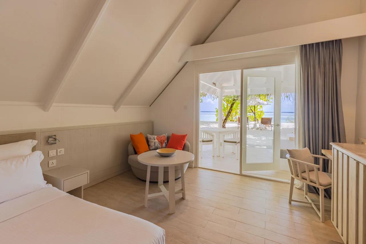 Interno della Family Beach Pavilion con letto e vista mare attraverso porta-finestra al LUX* South Ari Atoll.