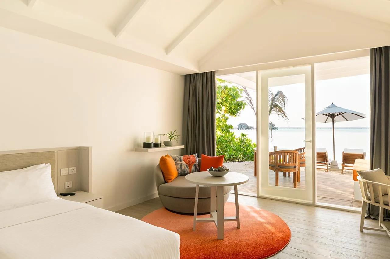 Interno della Family Lagoon Pavilion con divano, tavolino e vista su terrazza e lettini al LUX* South Ari Atoll.