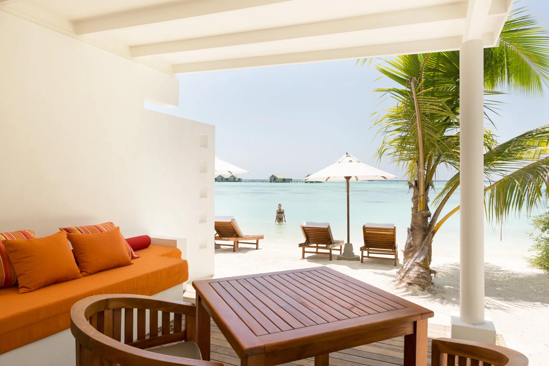 Terrazza della Family Lagoon Pavilion con divano, tavolo in legno e vista sulla spiaggia del LUX* South Ari Atoll.