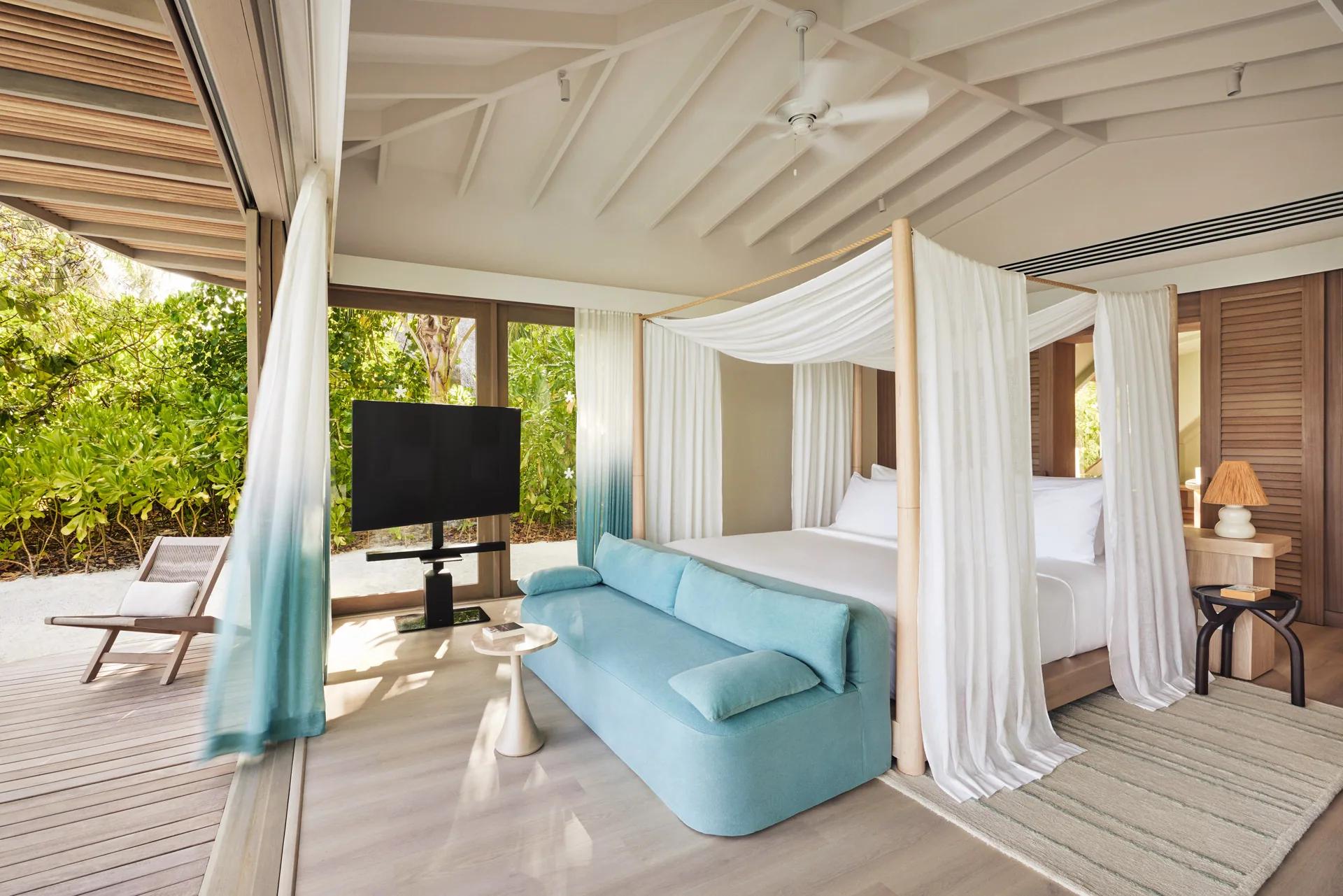 Interno della Temptation Beach Pool Villa con letto a baldacchino e divano azzurro al LUX* South Ari Atoll.