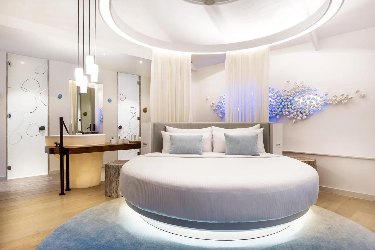 Interno della Temptation Pool Water Villa con letto rotondo, luci soffuse e decorazioni murali al LUX* South Ari Atoll.