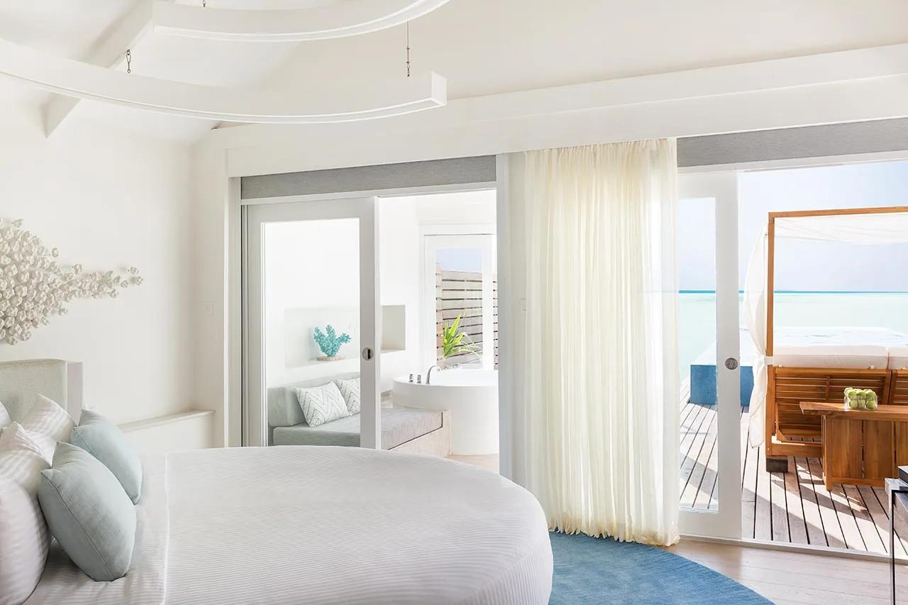 Interno della Temptation Pool Water Villa con letto, divano, vasca e terrazza vista mare al LUX* South Ari Atoll.