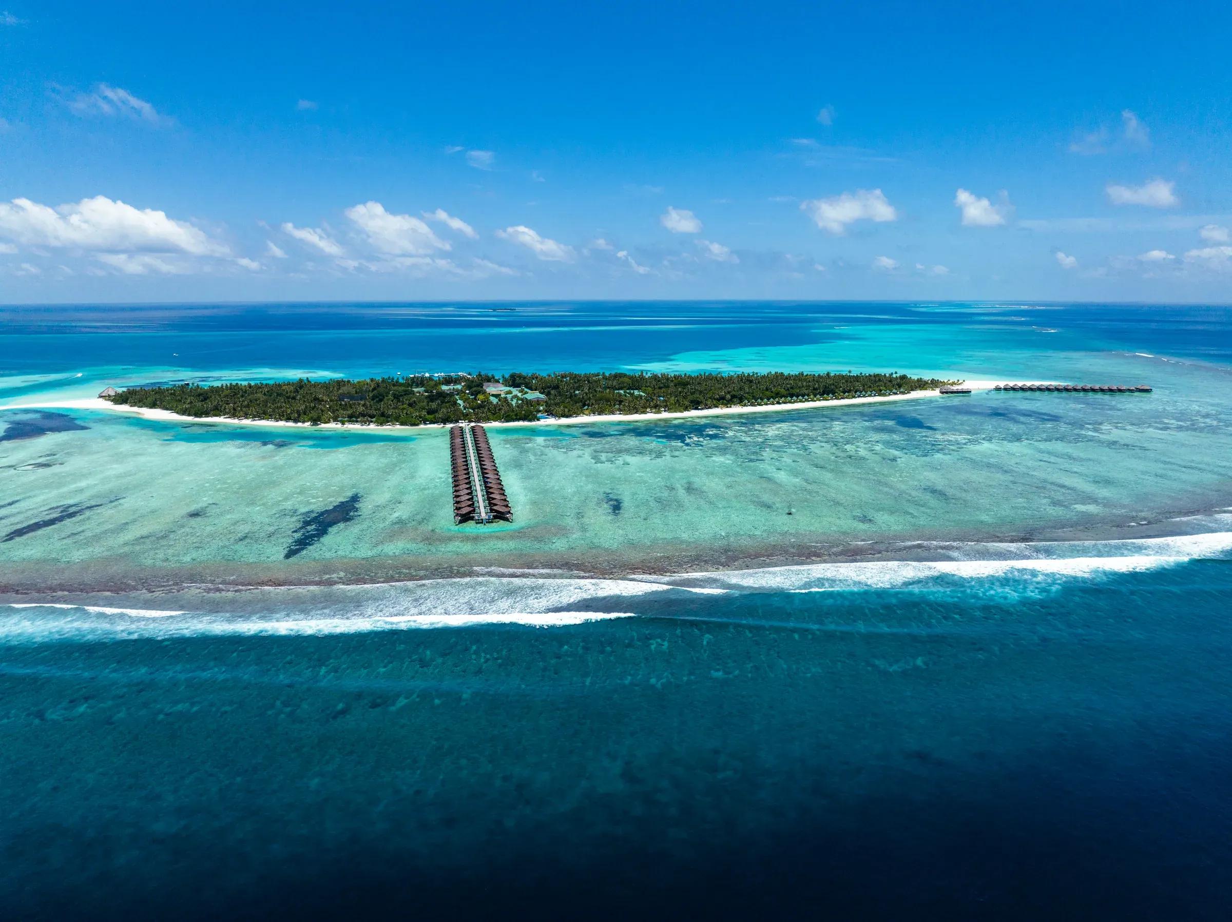 Vista aerea del Meeru Island Resort & Spa circondato da acqua turchese e barriera corallina.