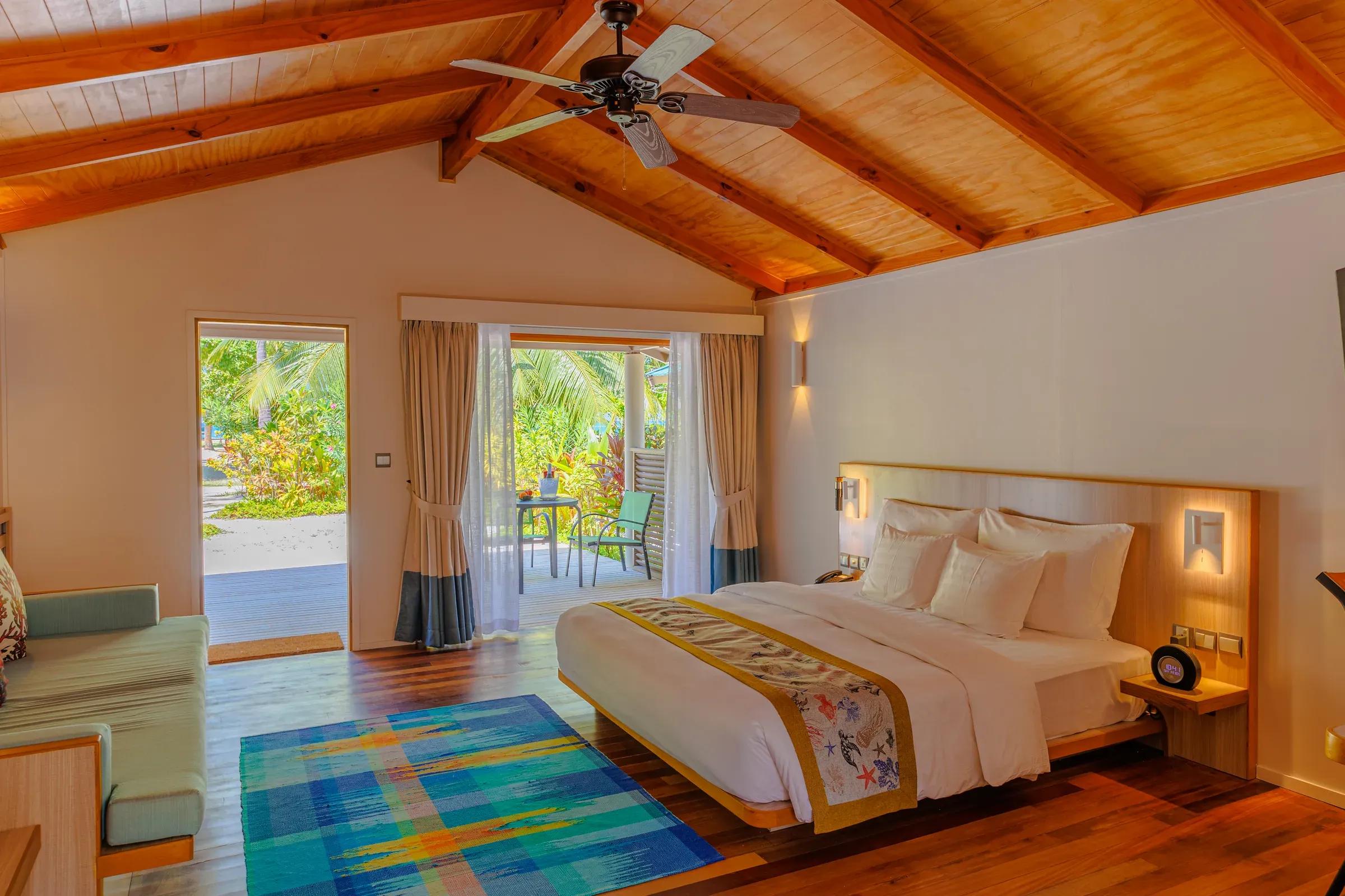 Interno della Family Villa con letto matrimoniale e patio con vista sulle palme del Meeru Island Resort & Spa.