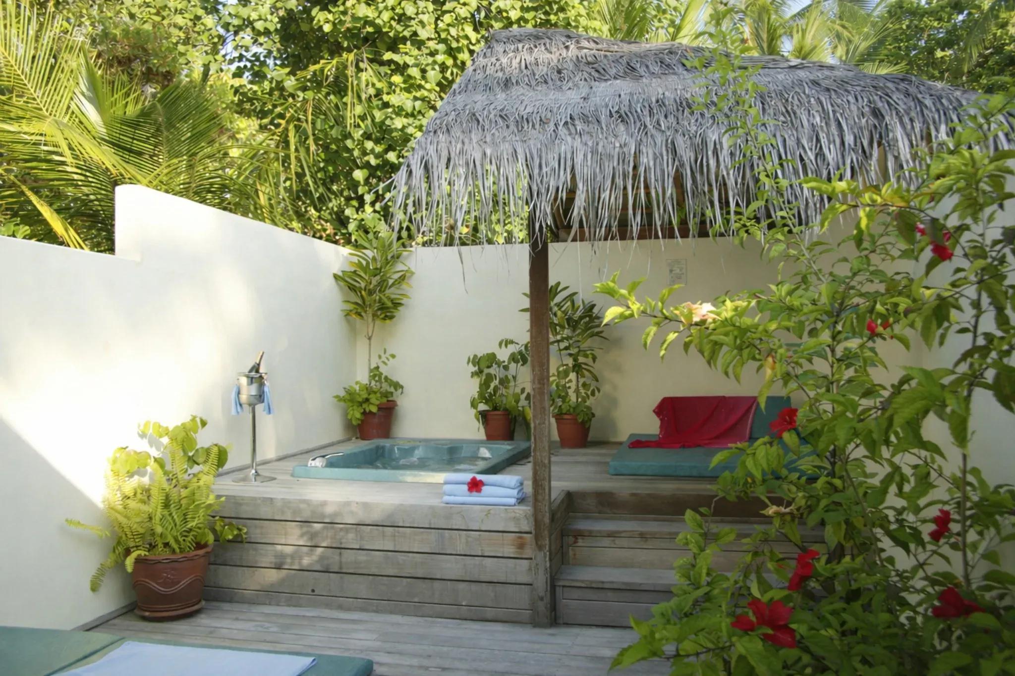 Area esterna della Jacuzzi Beach Villa con jacuzzi e vegetazione al Meeru Island Resort & Spa.