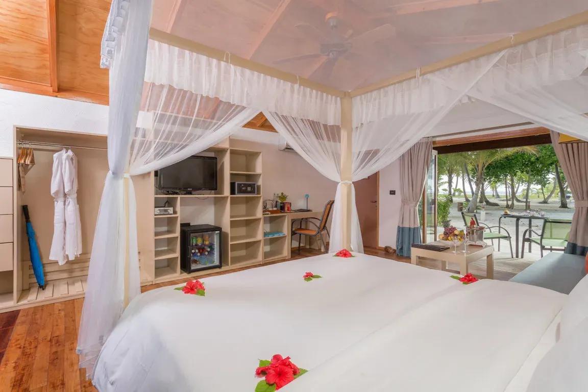 Interno della Jacuzzi Beach Villa con letto a baldacchino, TV e vista sulla spiaggia al Meeru Island Resort & Spa.