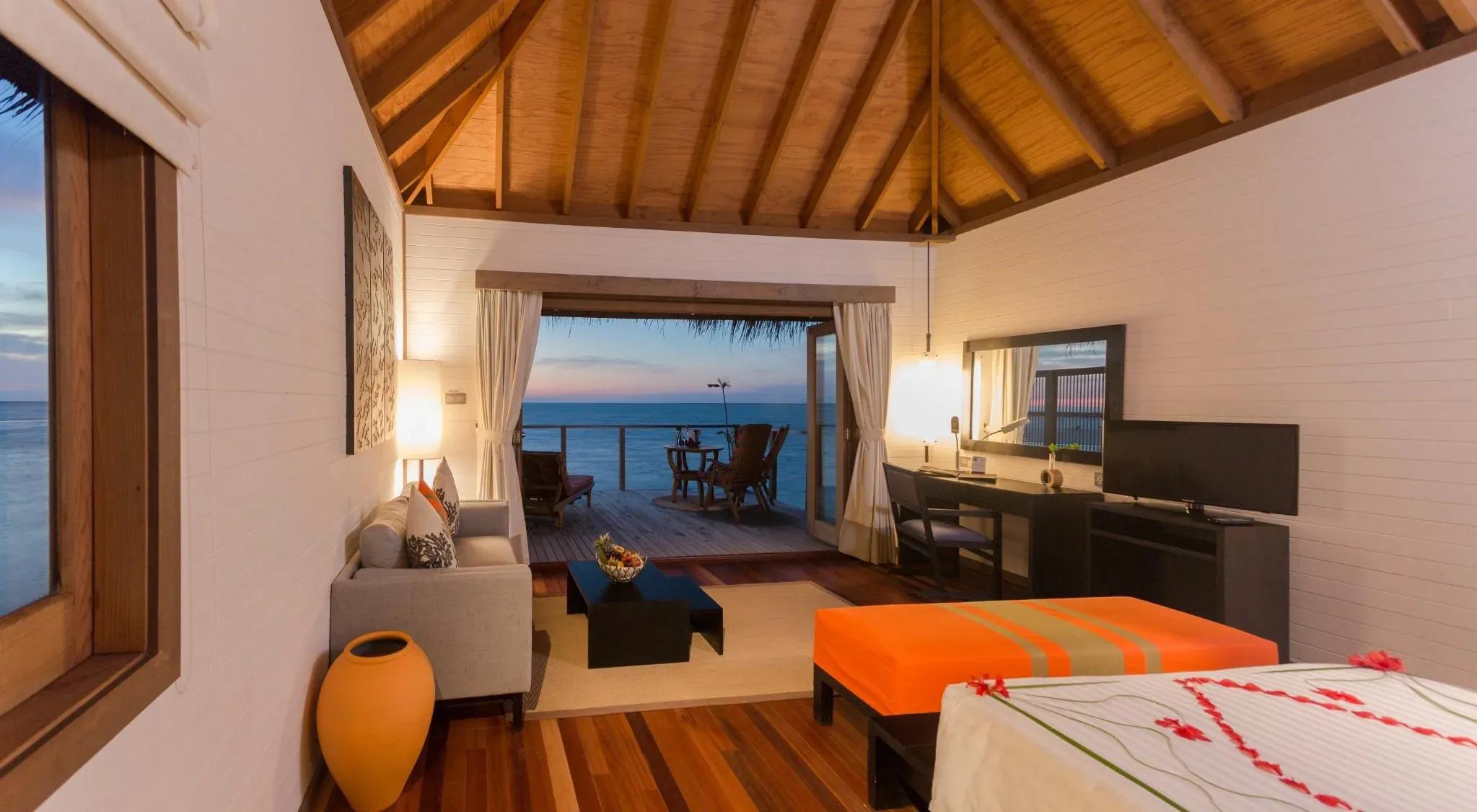 Interno della Jacuzzi Water Villa con divano, tavolo e vista sull'oceano al Meeru Island Resort & Spa.