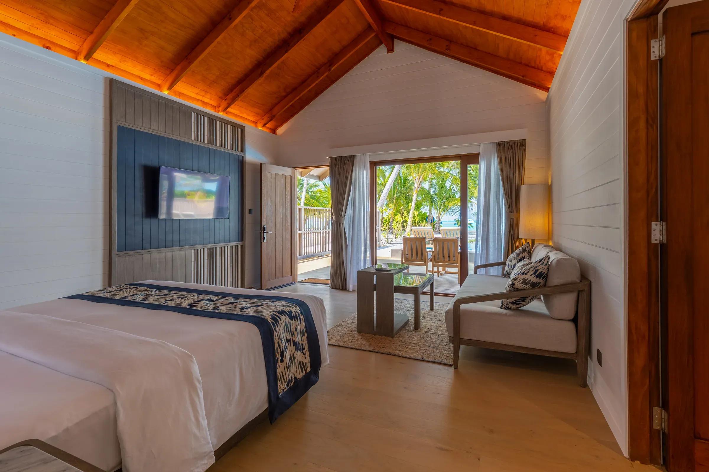 Interno della Two Bedroom Beach Pool Villa con letto, divano e accesso alla terrazza al Meeru Island Resort & Spa.