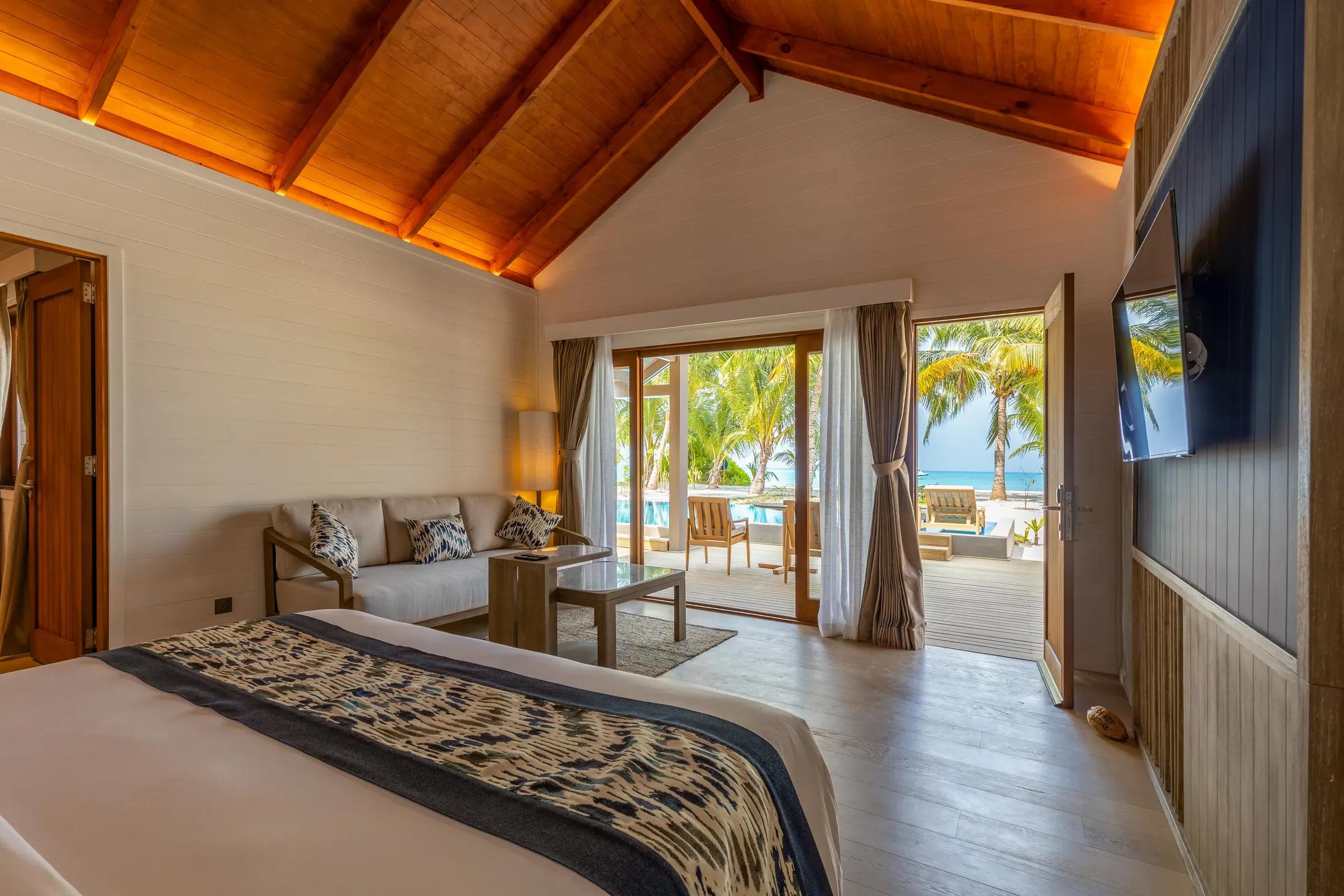 Interno della Two Bedroom Beach Pool Villa con vista su terrazza con sedie di legno e piscina al Meeru Island Resort & Spa.