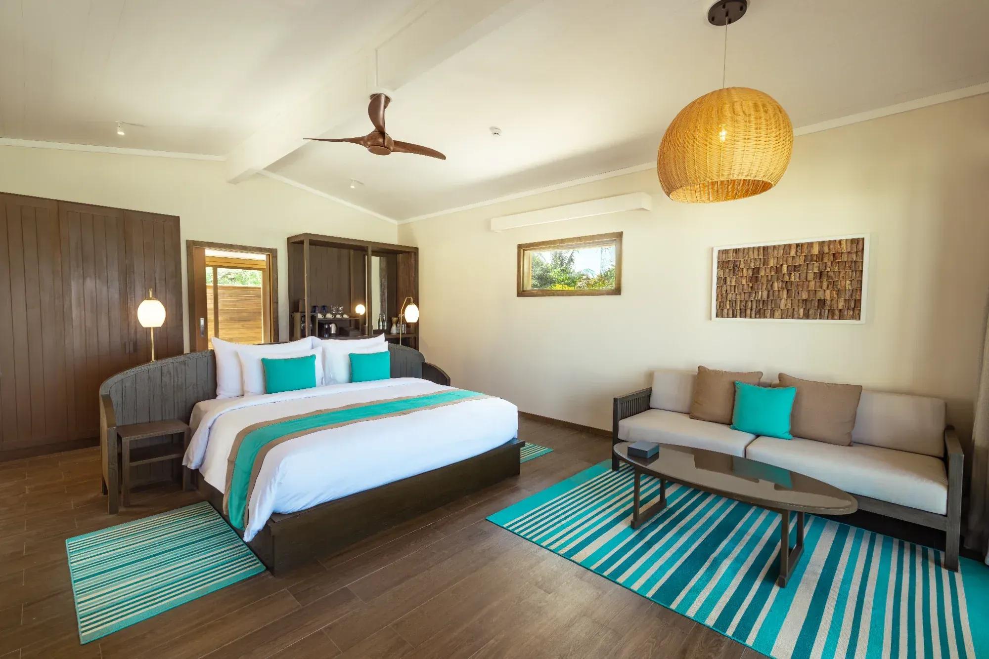 Interno della Romantic Beach Villa con letto matrimoniale, divano e decorazioni in legno al Nala Maldives By Jawakara.