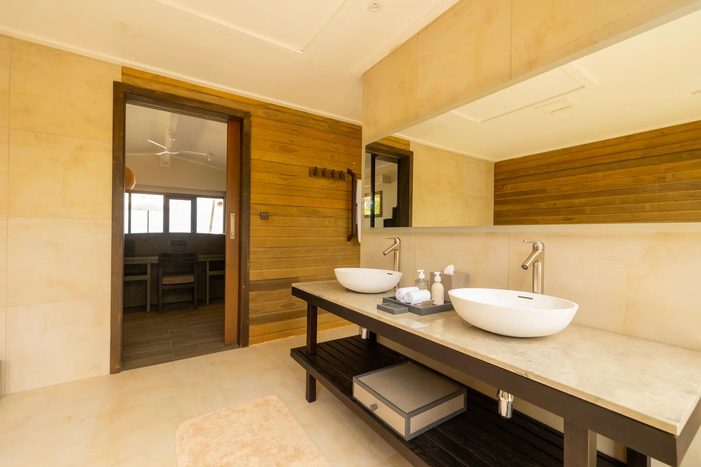 Bagno della Sunrise Beach Villa con lavandini doppi e arredi in legno al Nala Maldives By Jawakara.