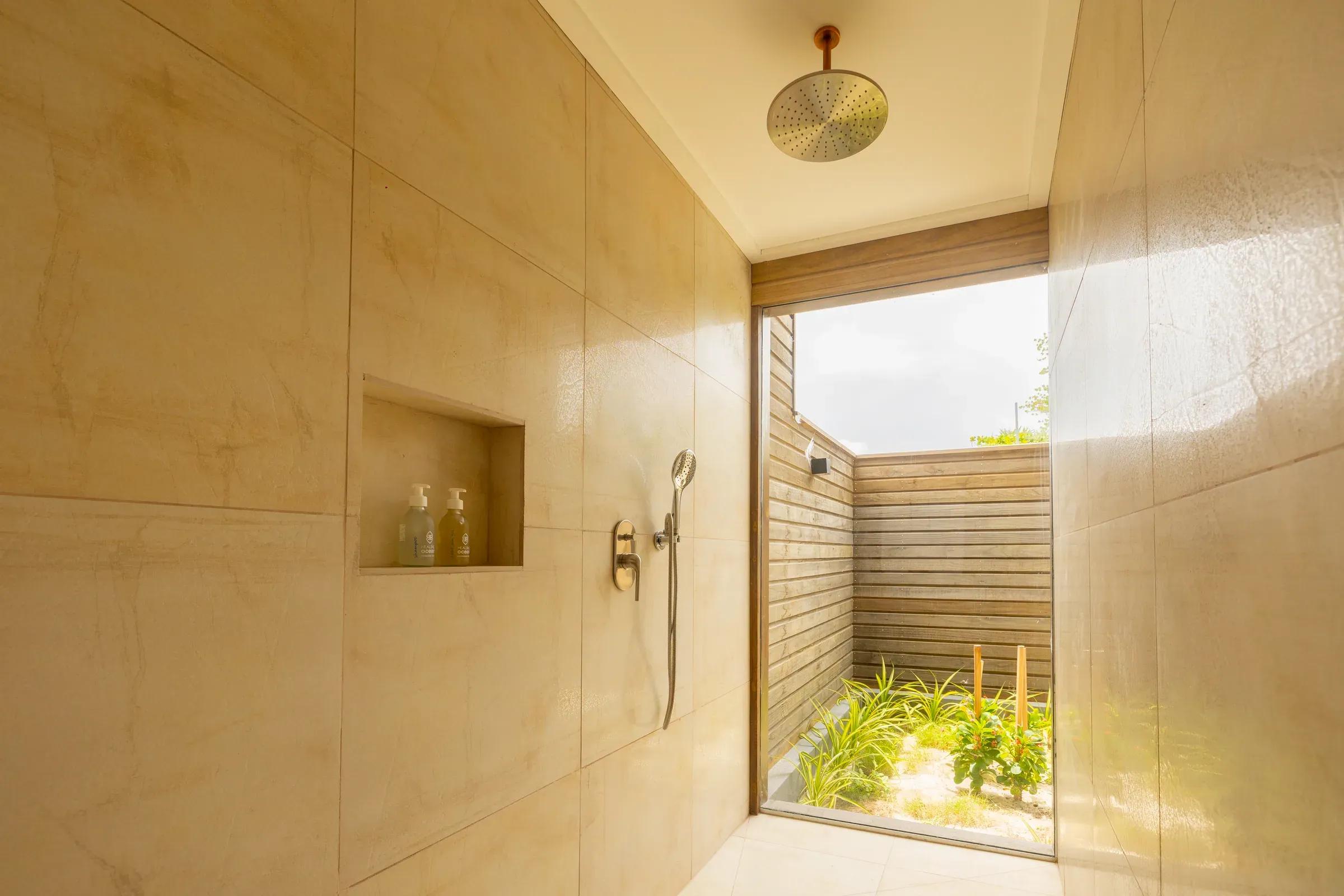 Bagno con doccia a pioggia e accesso a piccolo giardino nella Sunrise Beach Villa del Nala Maldives By Jawakara.