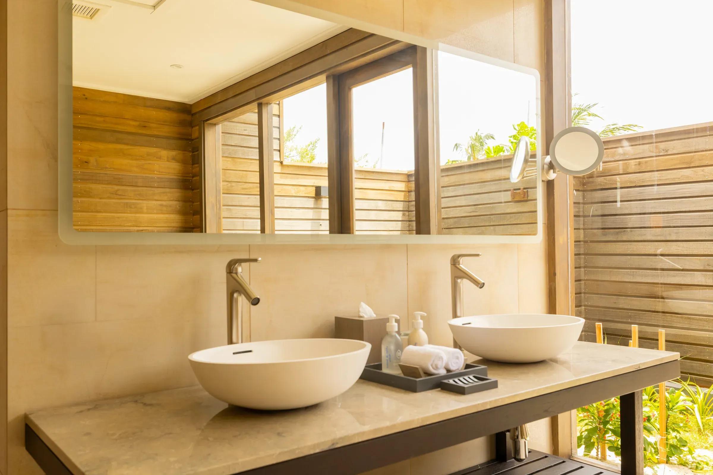 Bagno della Sunrise Beach Villa con doppio lavabo e vista su giardino privato al Nala Maldives By Jawakara.