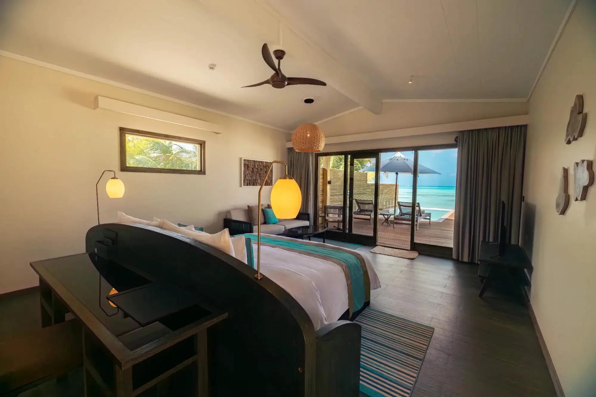 Interno della Sunset Beach Pool Villa con letto, lampada e vista sulla terrazza del Nala Maldives By Jawakara