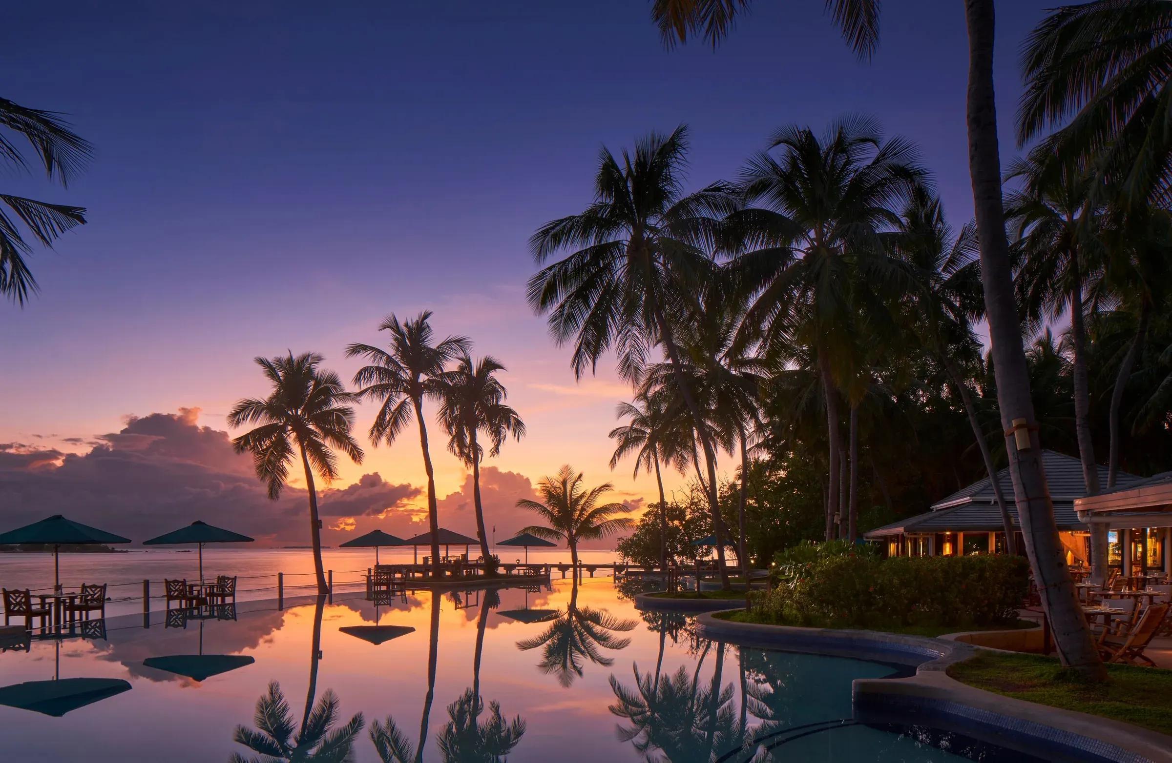 Piscina con palme e ombrelloni al tramonto presso il Royal Island Resort & Spa
