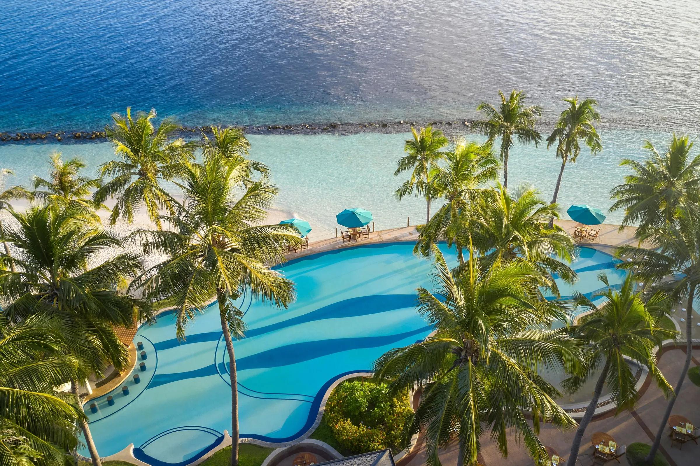 Piscina con palme e spiaggia con mare cristallino al Royal Island Resort & Spa alle Maldive.