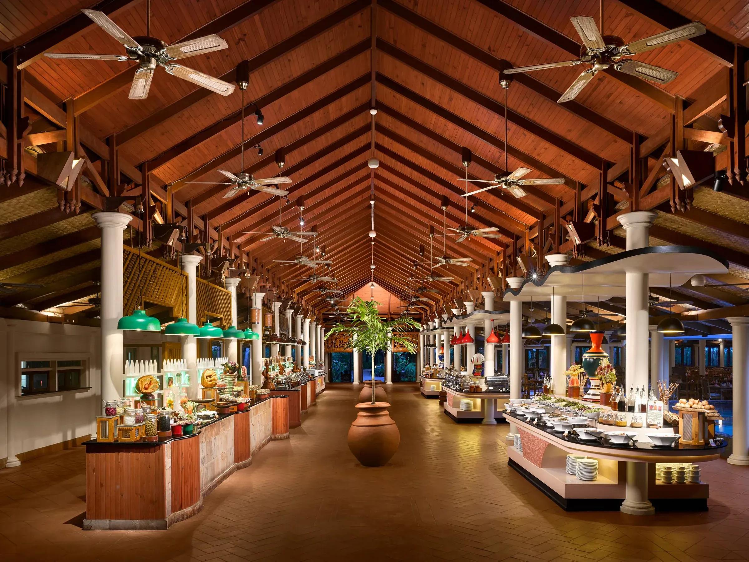 Elegante ristorante a buffet del Royal Island Resort & Spa con alti soffitti in legno, che offre una vasta selezione di cucina internazionale in un'atmosfera tropicale.