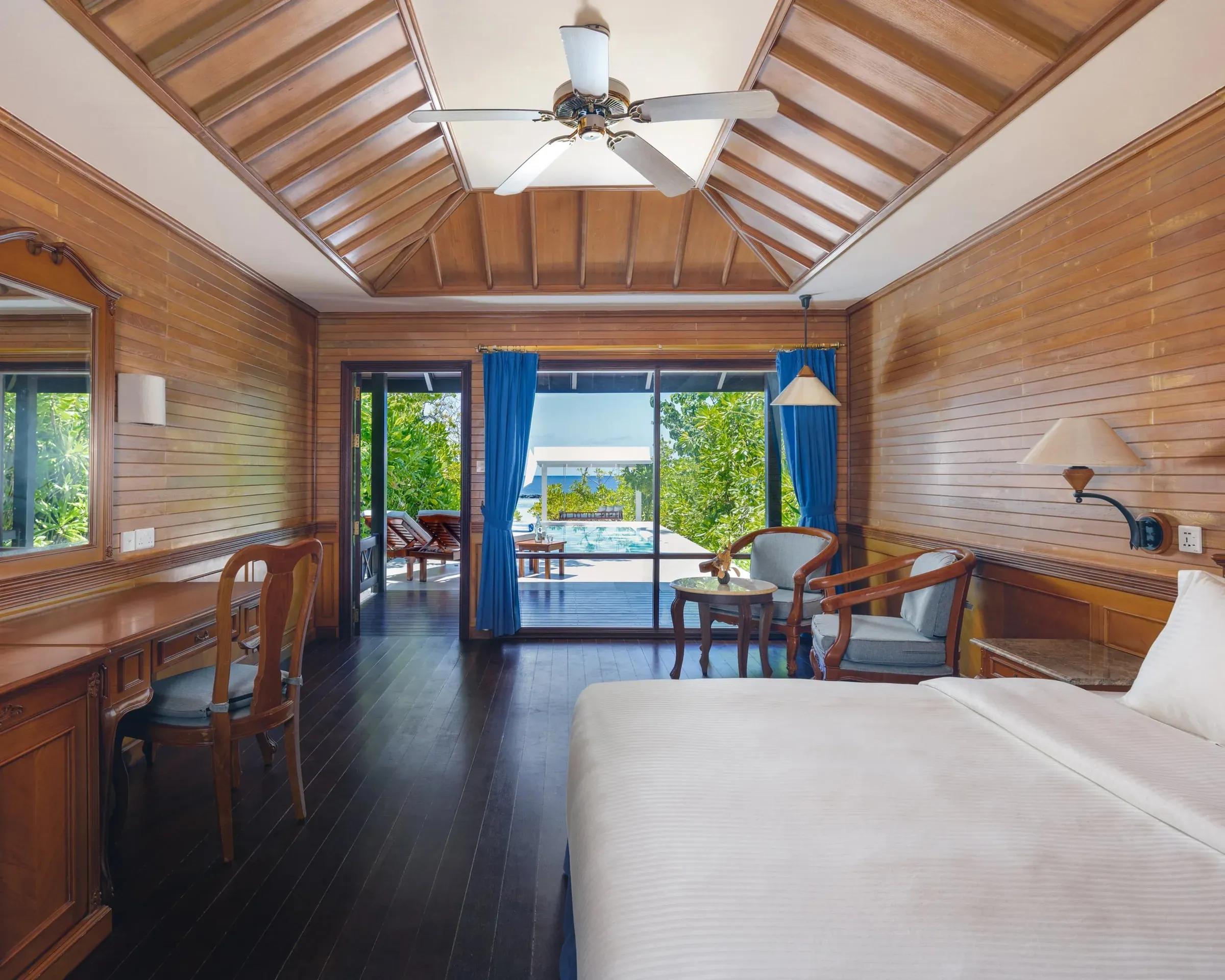 Interno lussuoso della Beach Pool Villa al Royal Island Resort & Spa, con arredi in legno pregiato, un comodo letto e accesso diretto alla terrazza con piscina privata e vista sulla spiaggia.