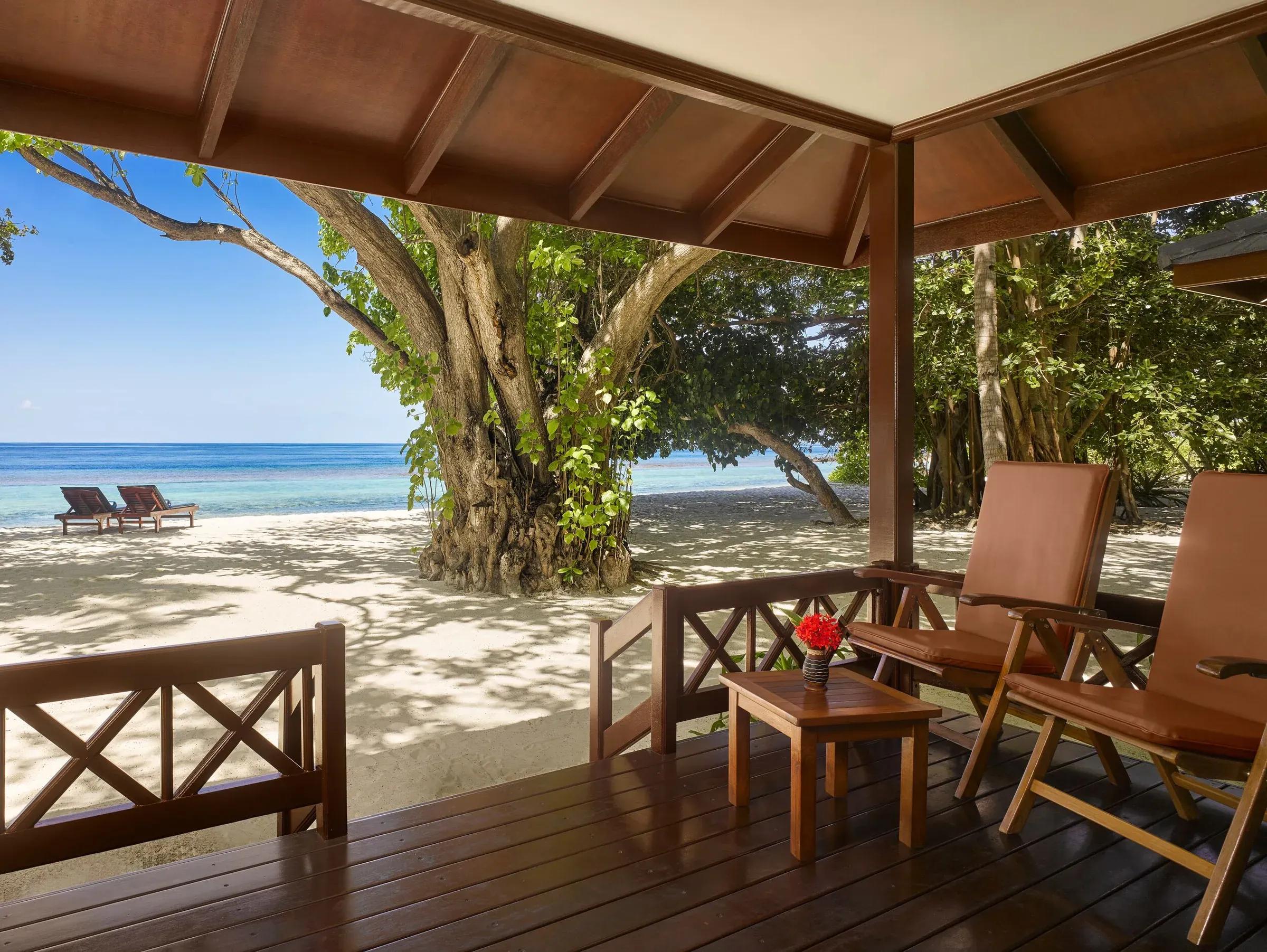 Terrazza privata in legno della Beach Villa con accesso diretto alla spiaggia di sabbia bianca, vista sull'oceano turchese e sulla lussureggiante vegetazione tropicale del Royal Island Resort & Spa.