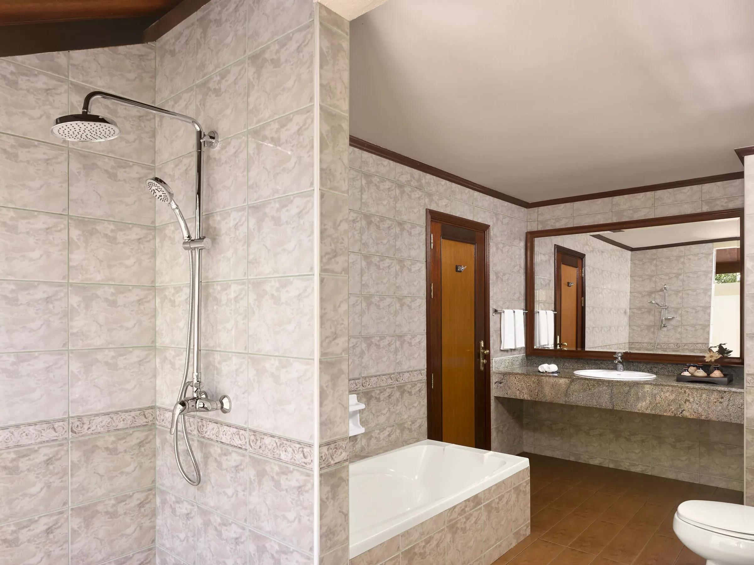 Bagno con vasca e doccia della Sunset Beach Villa al Royal Island Resort & Spa, piastrelle in marmo e lavandino.