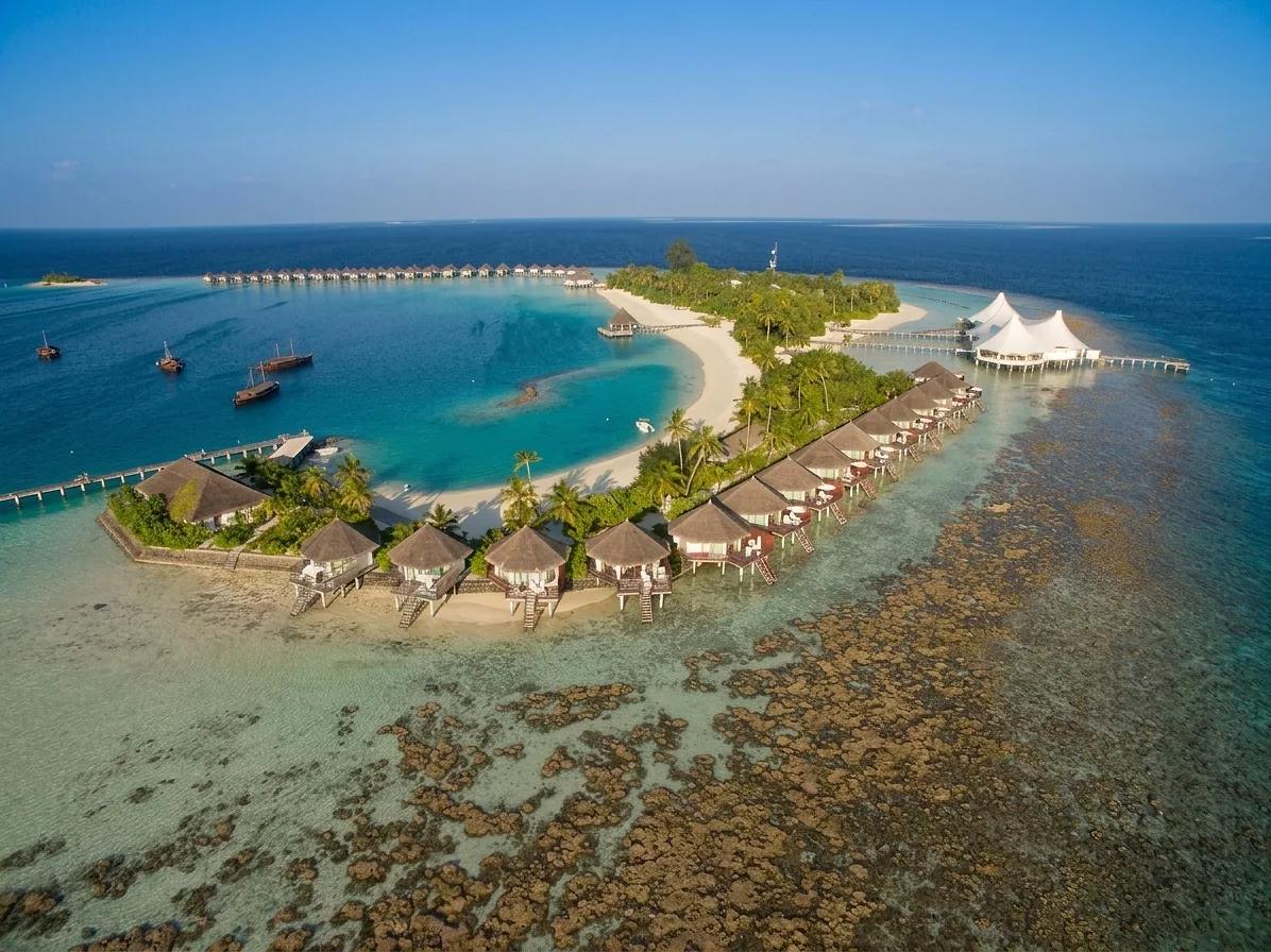 Veduta aerea del Safari Island Resort alle Maldive, un'isola con bungalow sull'acqua, spiagge bianche, una laguna turchese e la barriera corallina visibile nel mare cristallino.