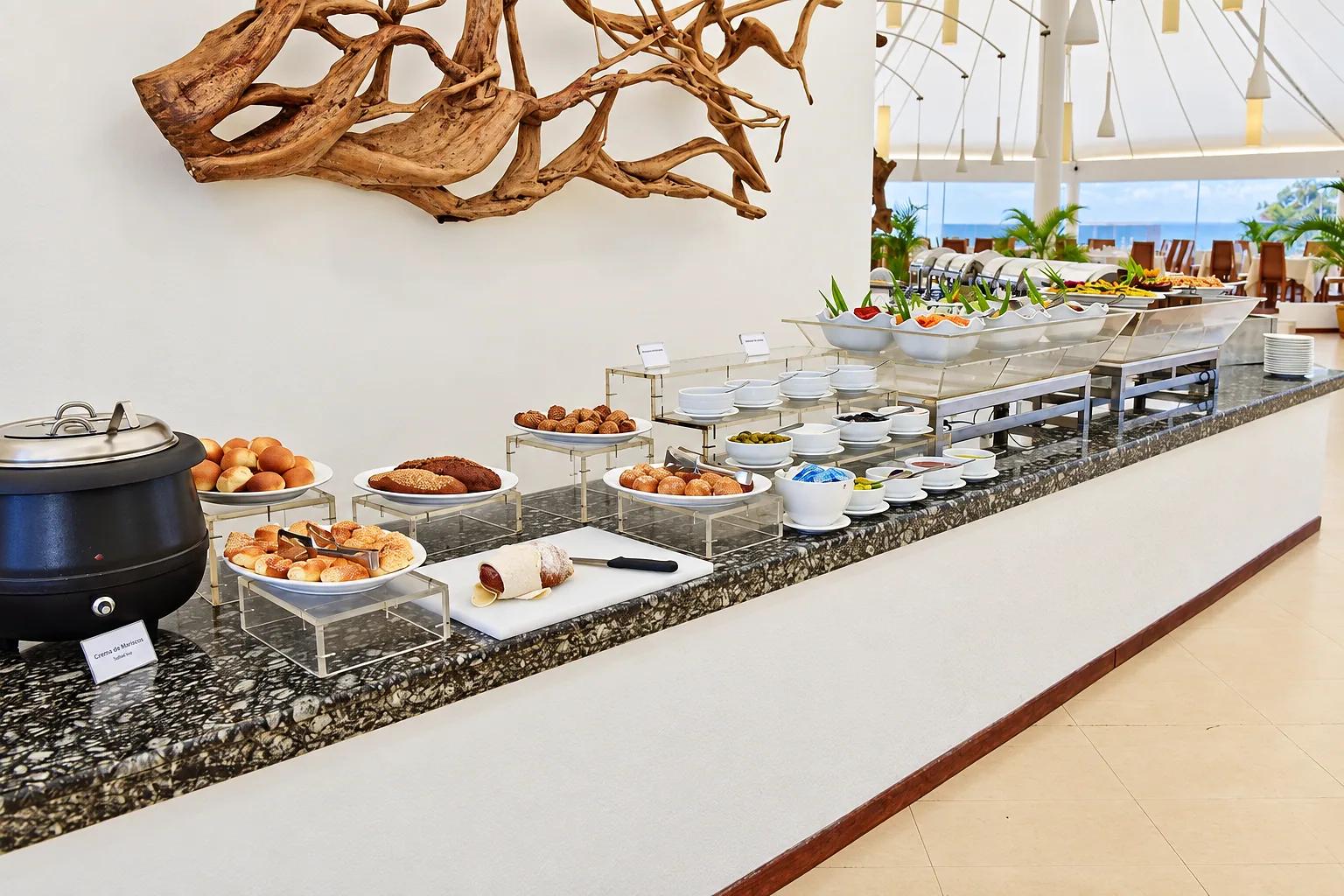 Il buffet del ristorante al Safari Island Resort, allestito su un bancone in marmo con un'ampia scelta di pane, salumi, insalate e piatti caldi in una sala luminosa con vista mare.