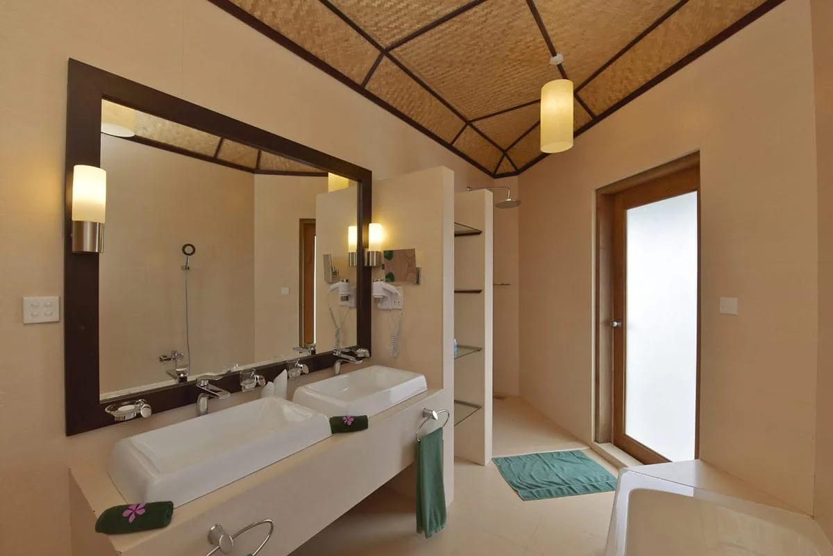 Il bagno del Beach Bungalow al Safari Island Resort, con doppio lavabo, vasca e doccia separata. L'ambiente è luminoso, con un alto soffitto a falde rivestito in materiale naturale intrecciato.