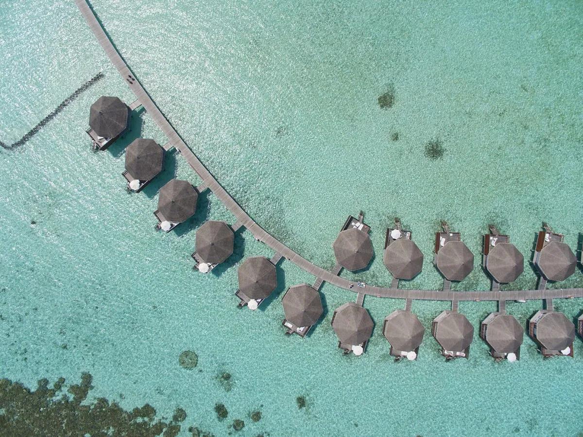 Vista aerea dei Water Bungalow del Safari Island Resort, disposti ad arco su una passerella che si estende sull'acqua cristallina della laguna.