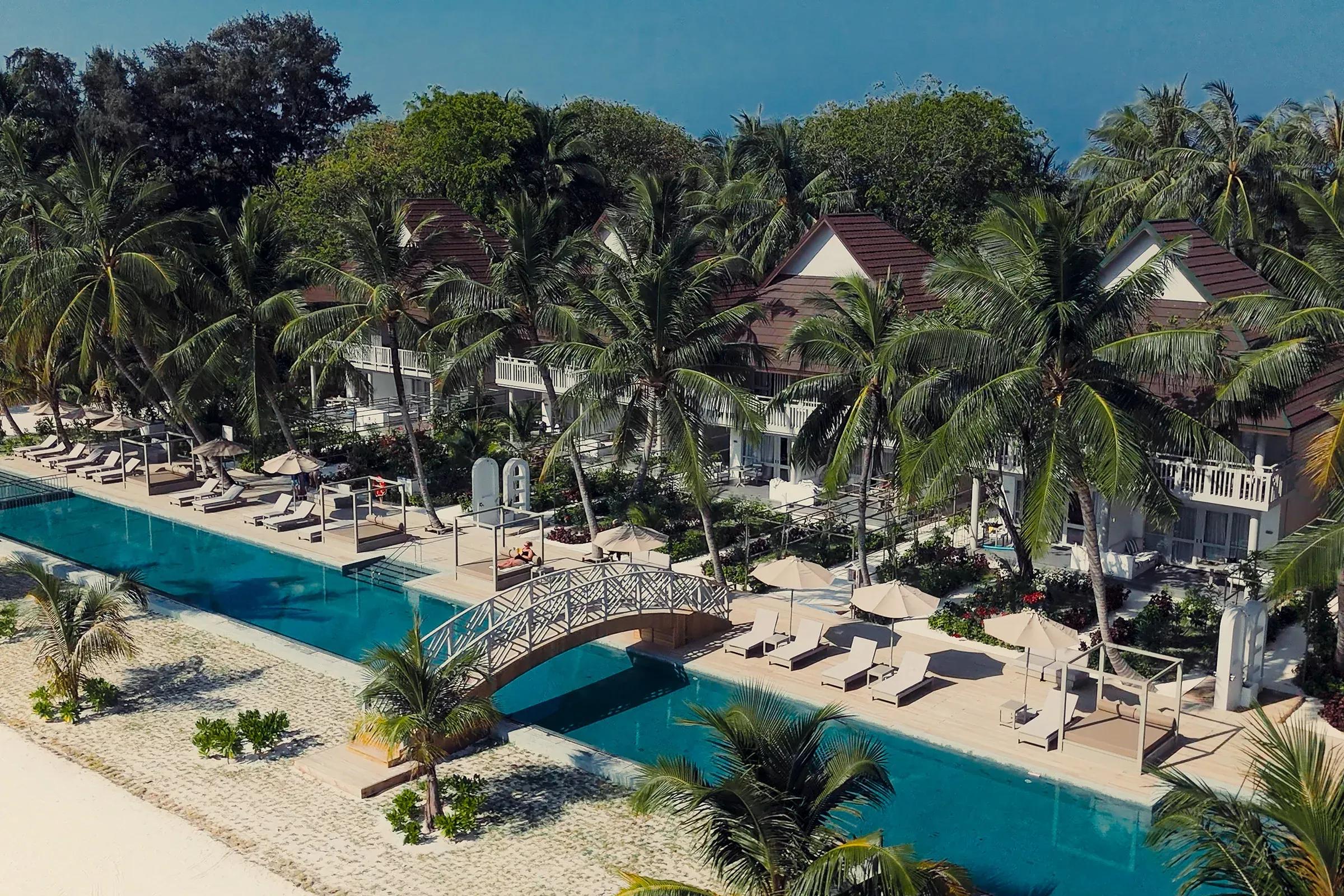Piscina con ponte circondata da lettini e palme al Sun Siyam Olhuveli.