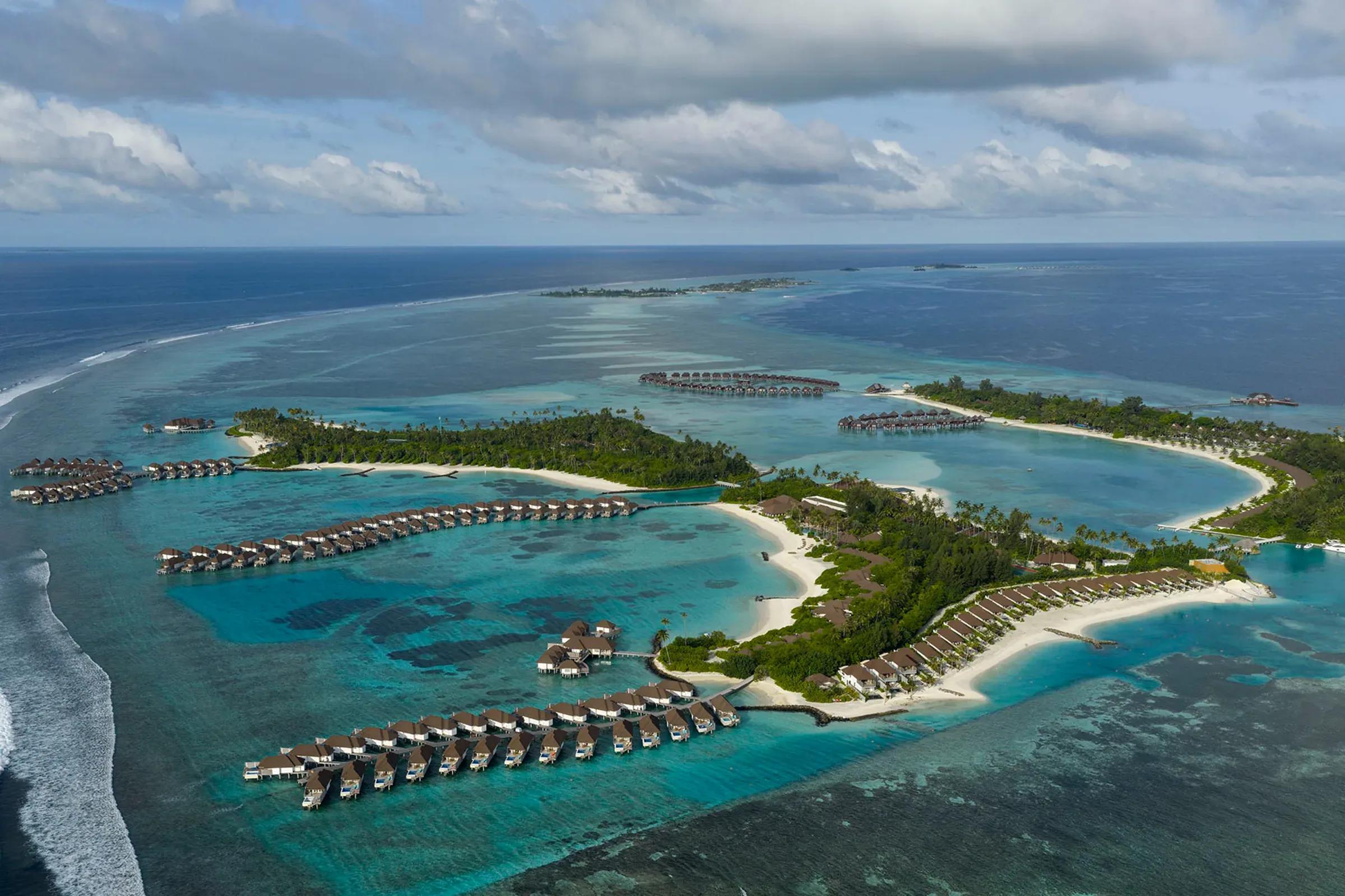 Vista aerea del Sun Siyam Olhuveli con ville sull'acqua e tre isole circondate da laguna turchese.