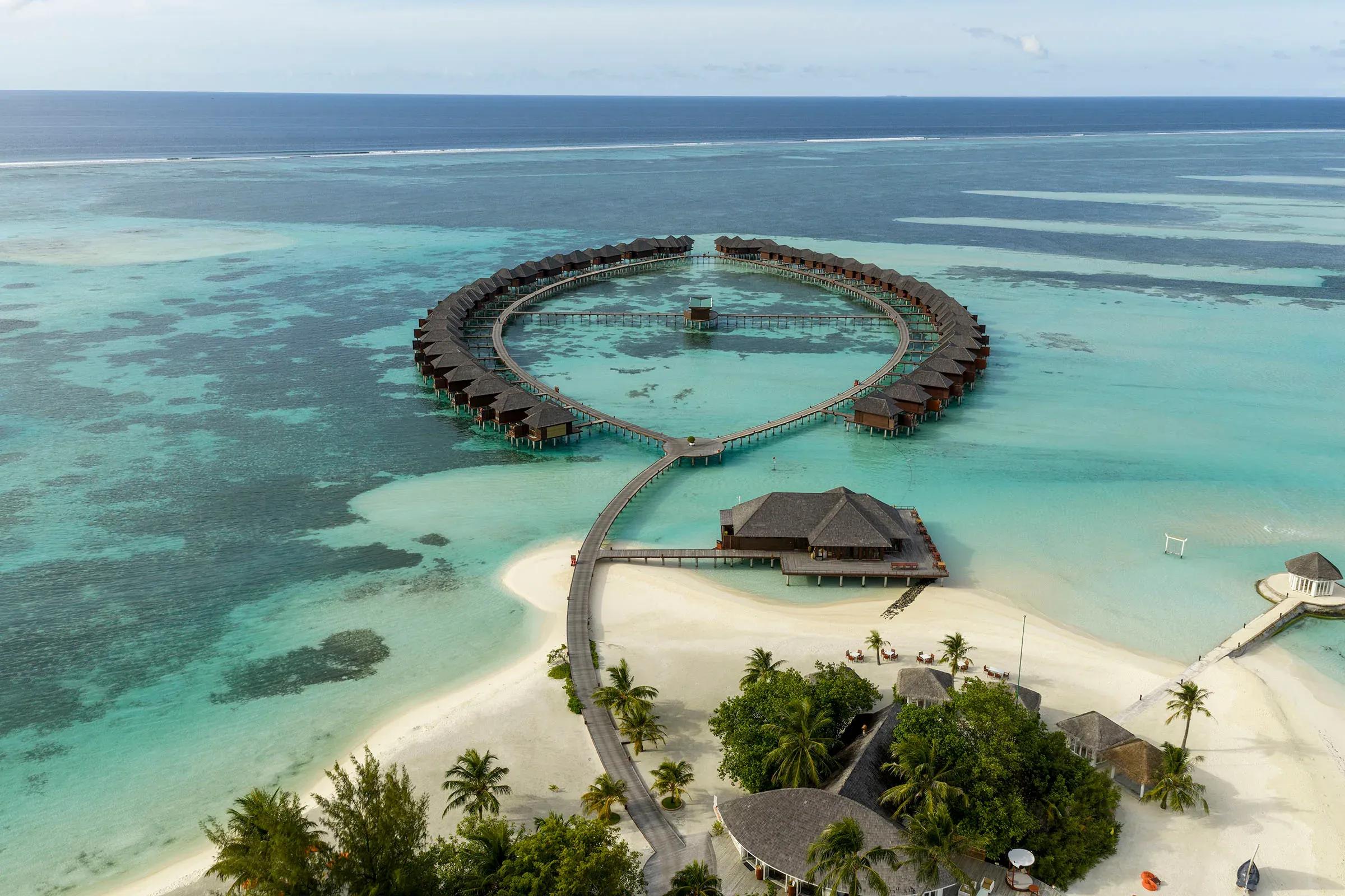 Villa sull'acqua disposte a forma di cuore e spiaggia con palme al Sun Siyam Olhuveli.