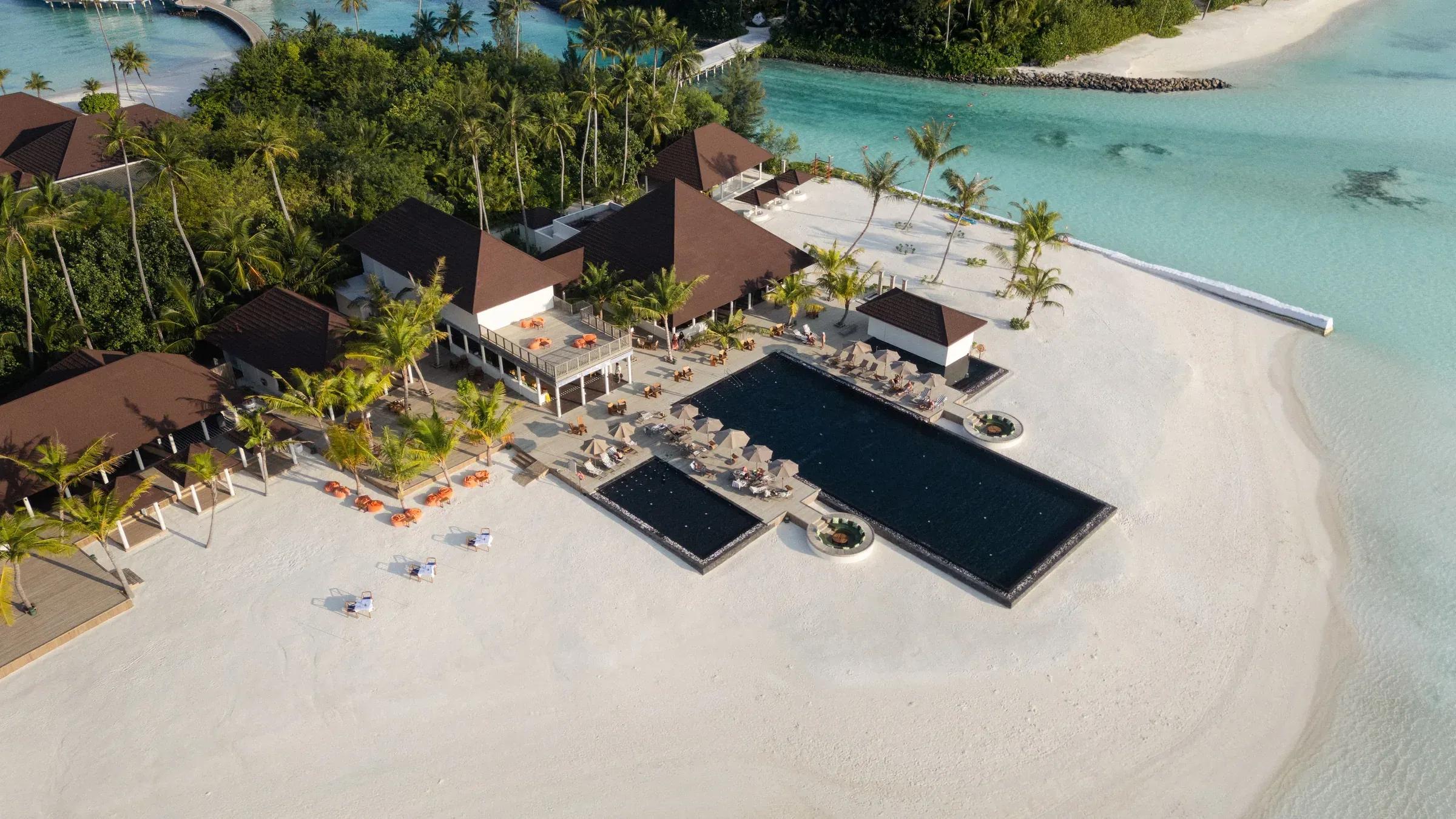 Piscina e spiaggia con lettini e palme al Sun Siyam Olhuveli.