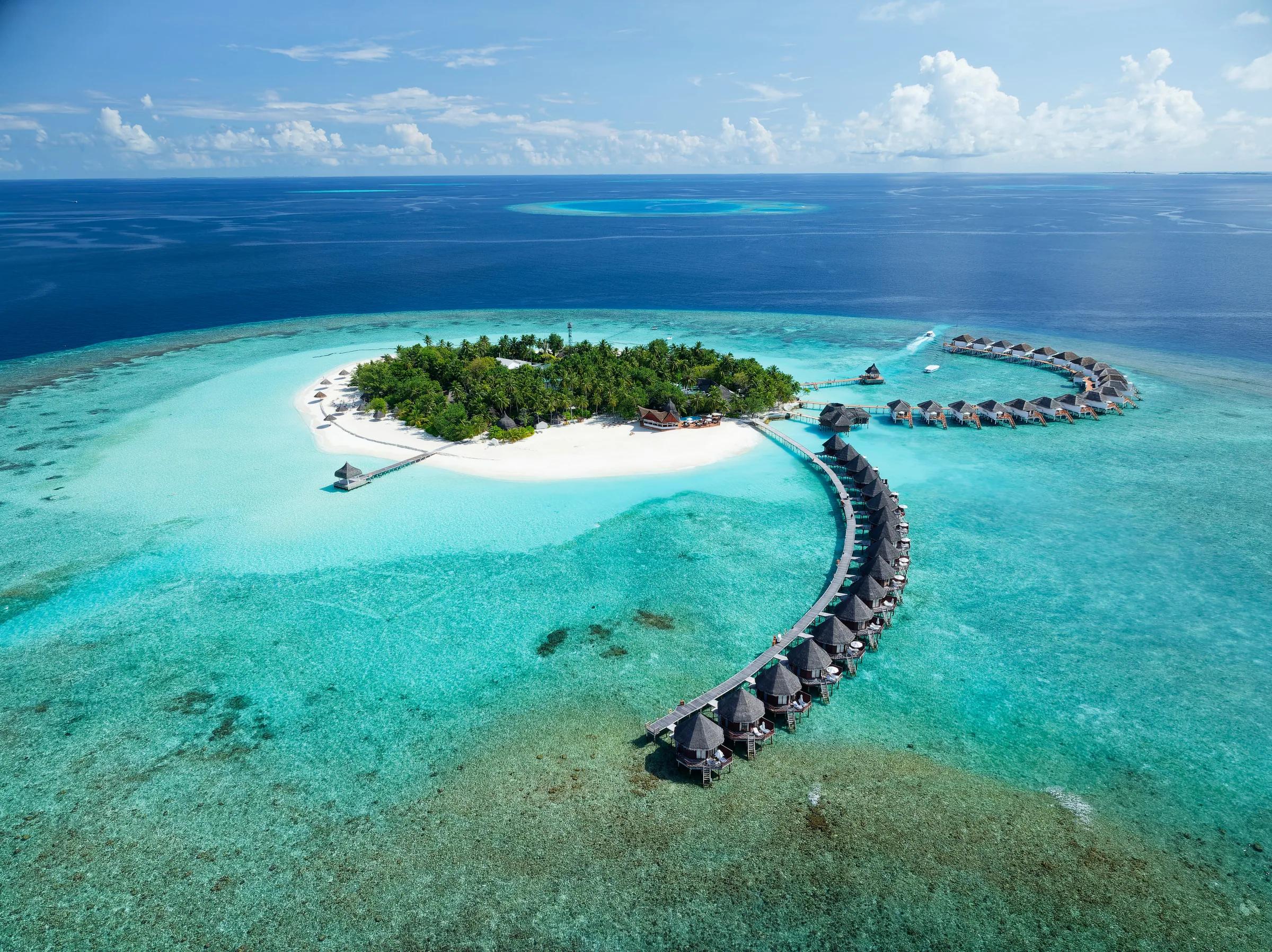 Veduta aerea del Thulhagiri Island Resort & Spa con bungalow sull'acqua e spiaggia bianca.