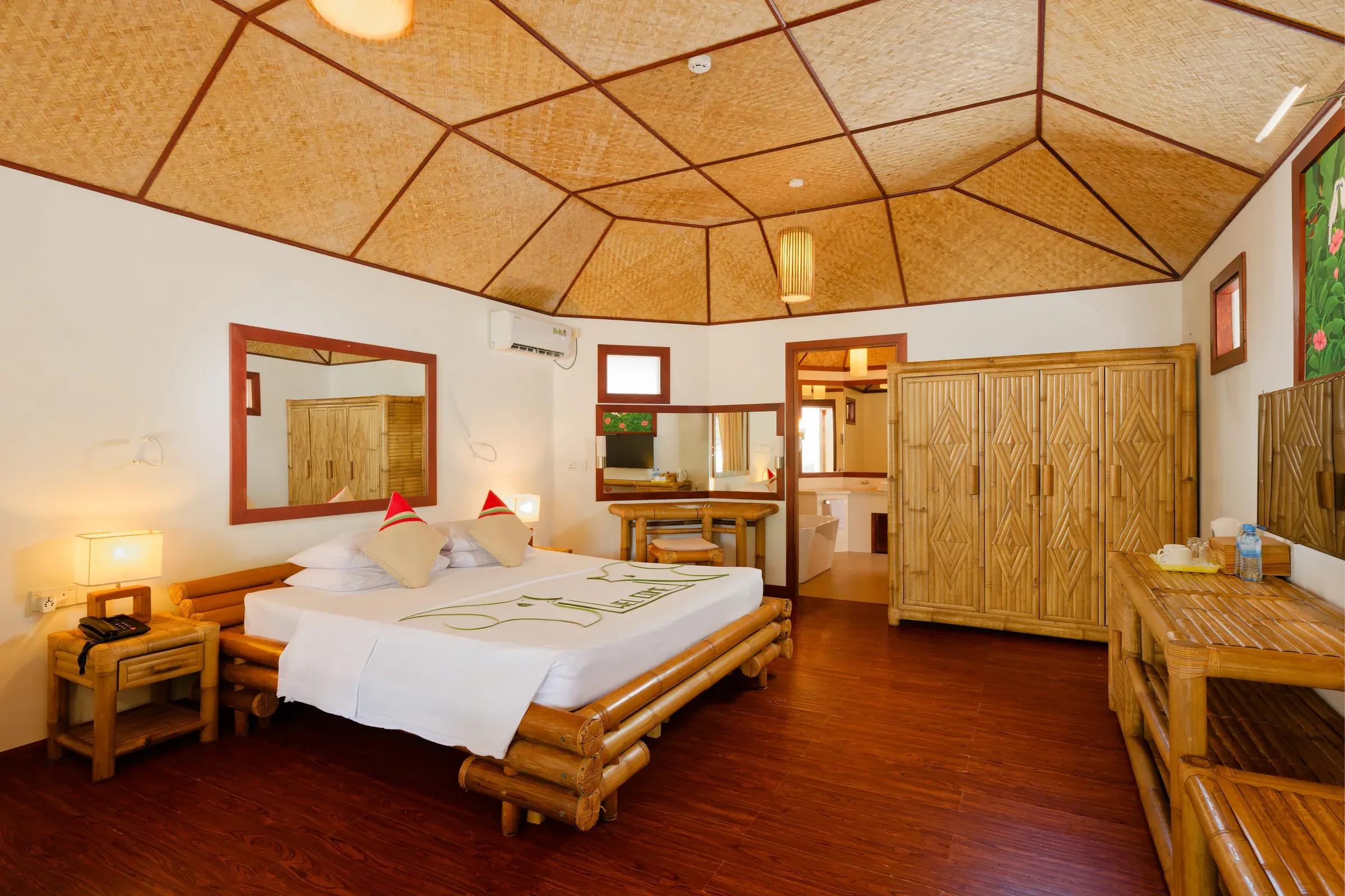 Interno del Beach Bungalow con letto matrimoniale e arredamento in legno presso il Thulhagiri Island Resort & Spa.