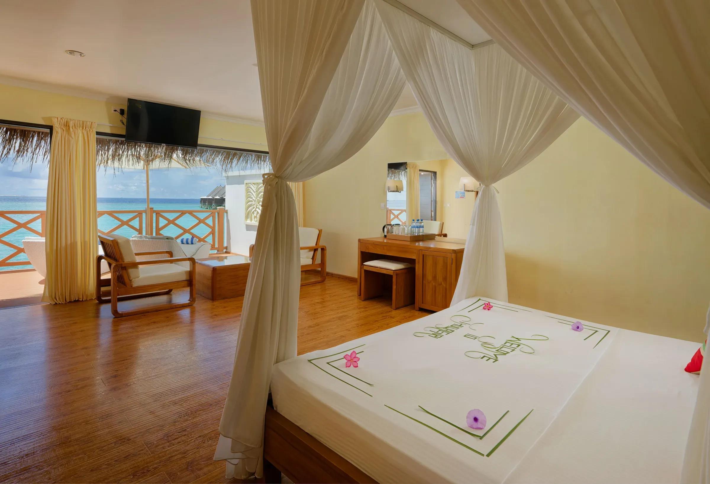 Interno della Superior Water Bungalow con letto a baldacchino e terrazza con vista mare al Thulhagiri Island Resort & Spa.