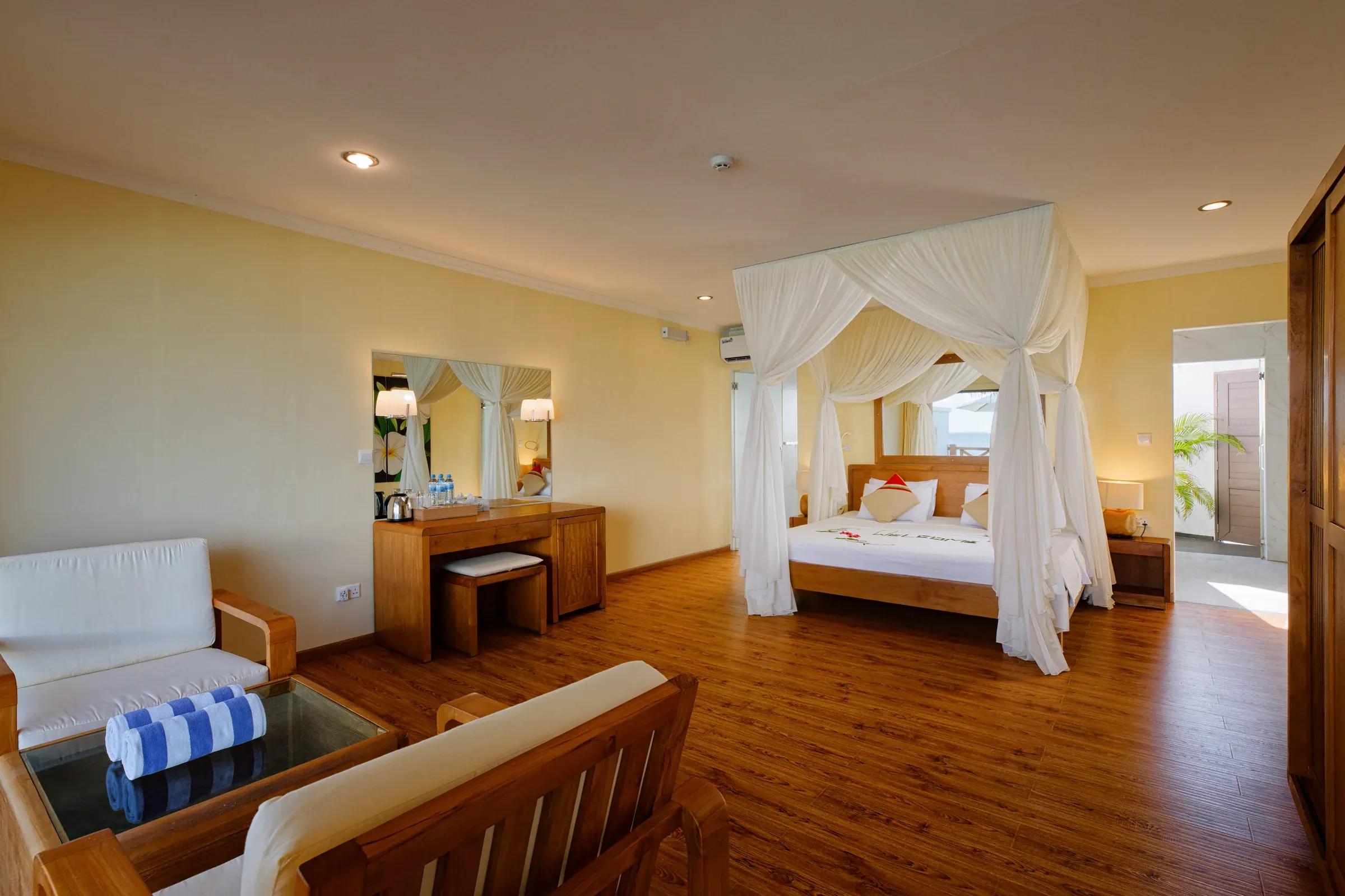 Interno di Superior Water Bungalow con letto a baldacchino e area salotto al Thulhagiri Island Resort & Spa.