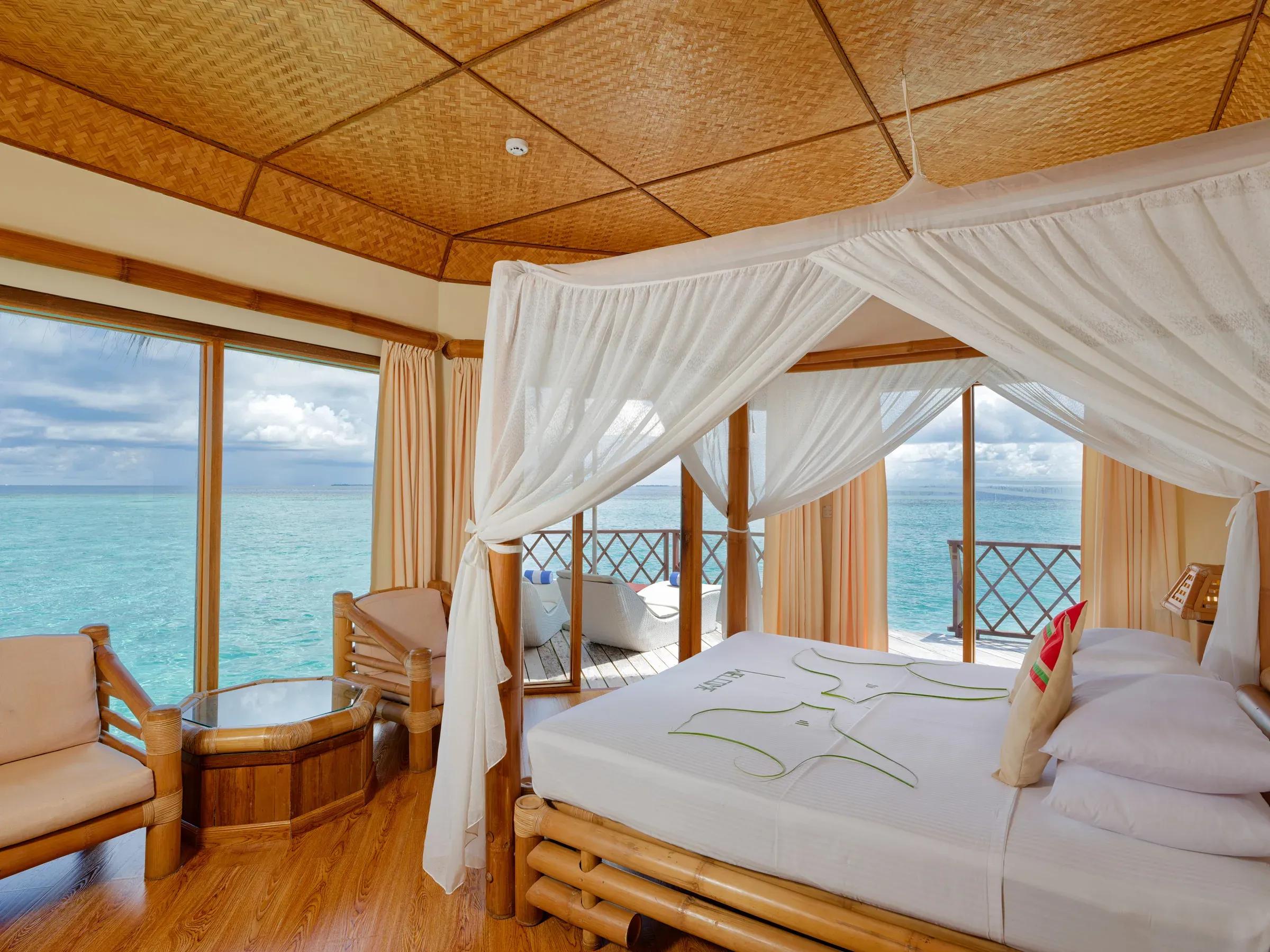 Interno del Water Bungalow con letto a baldacchino e vista sull'oceano del Thulhagiri Island Resort & Spa.